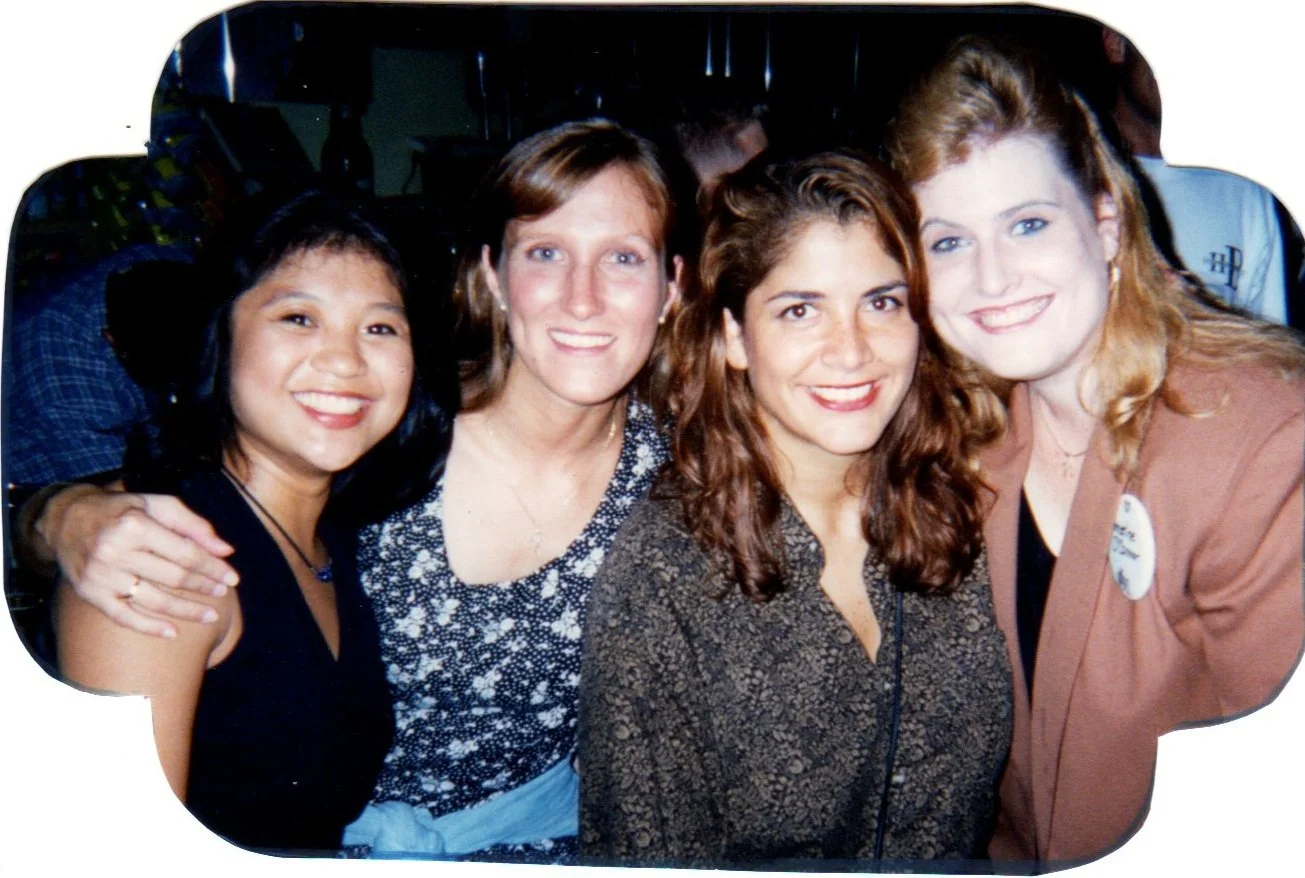 Four women smiling closely together at a social event.