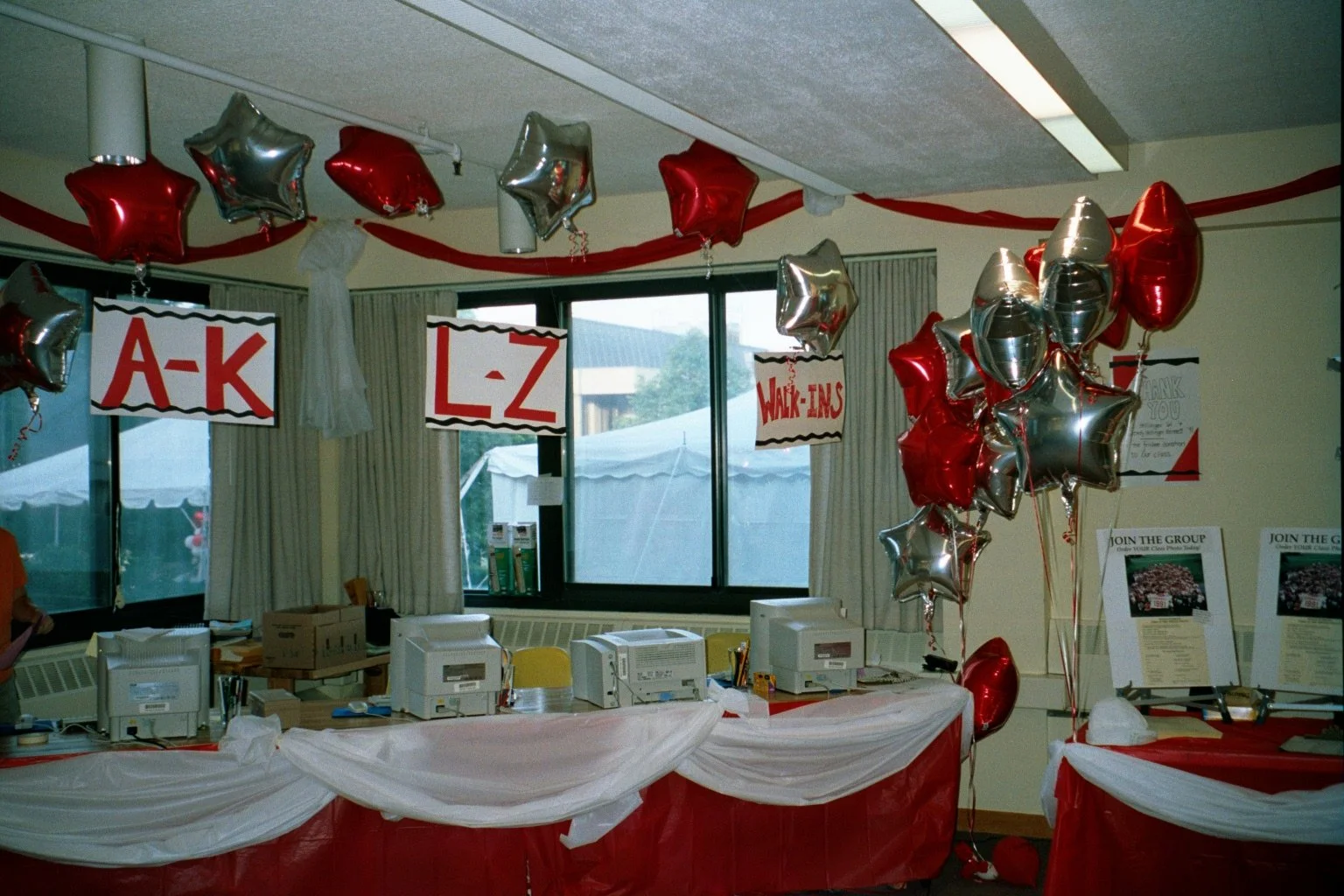 Decorated registration area with red and silver star-shaped balloons, signs categorizing alphabet groups for a walk-in event, and registration tables with computers, draped in red and white fabric.