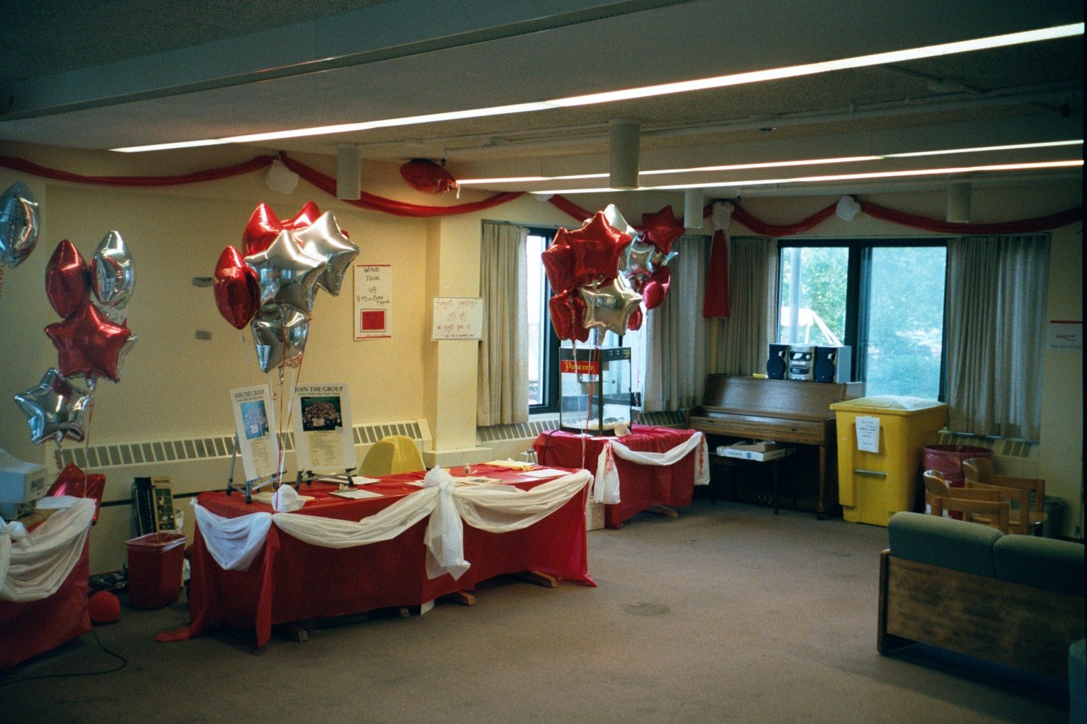 Room decorated for a celebration with red, white, and silver star-shaped balloons, with tables draped in red and white cloths, and informational signs on display.