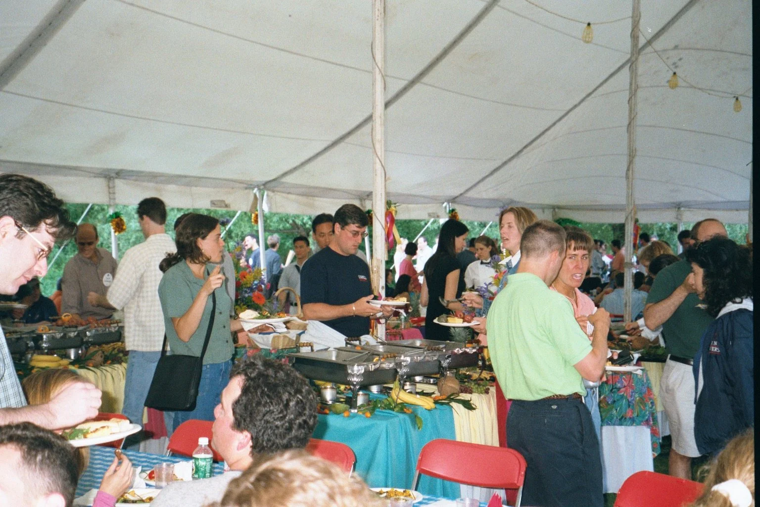 People at a buffet line under a large white tent, serving and eating food at a Class of 1991 dinner even during Reunion weekend.