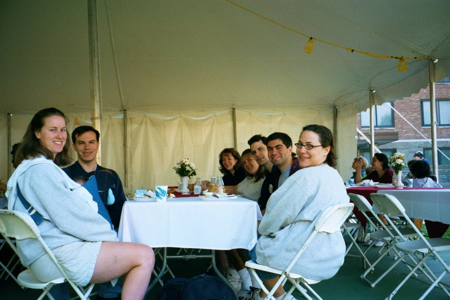 Group of people sitting at a long table under a tent, smiling and enjoying a meal together.