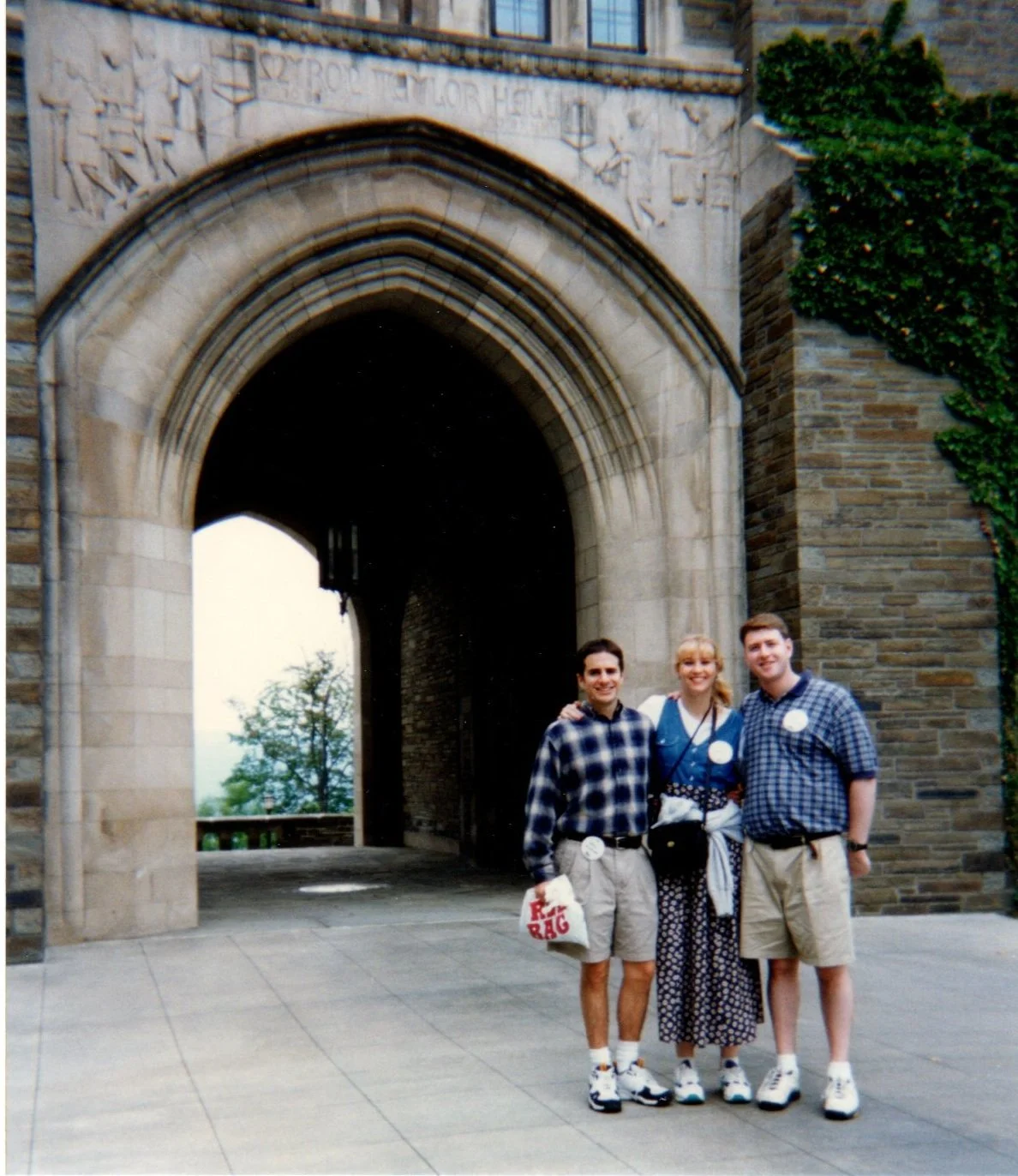 Three friends standing together smiling in front of an arched stone gate, with ivy growing on the side.