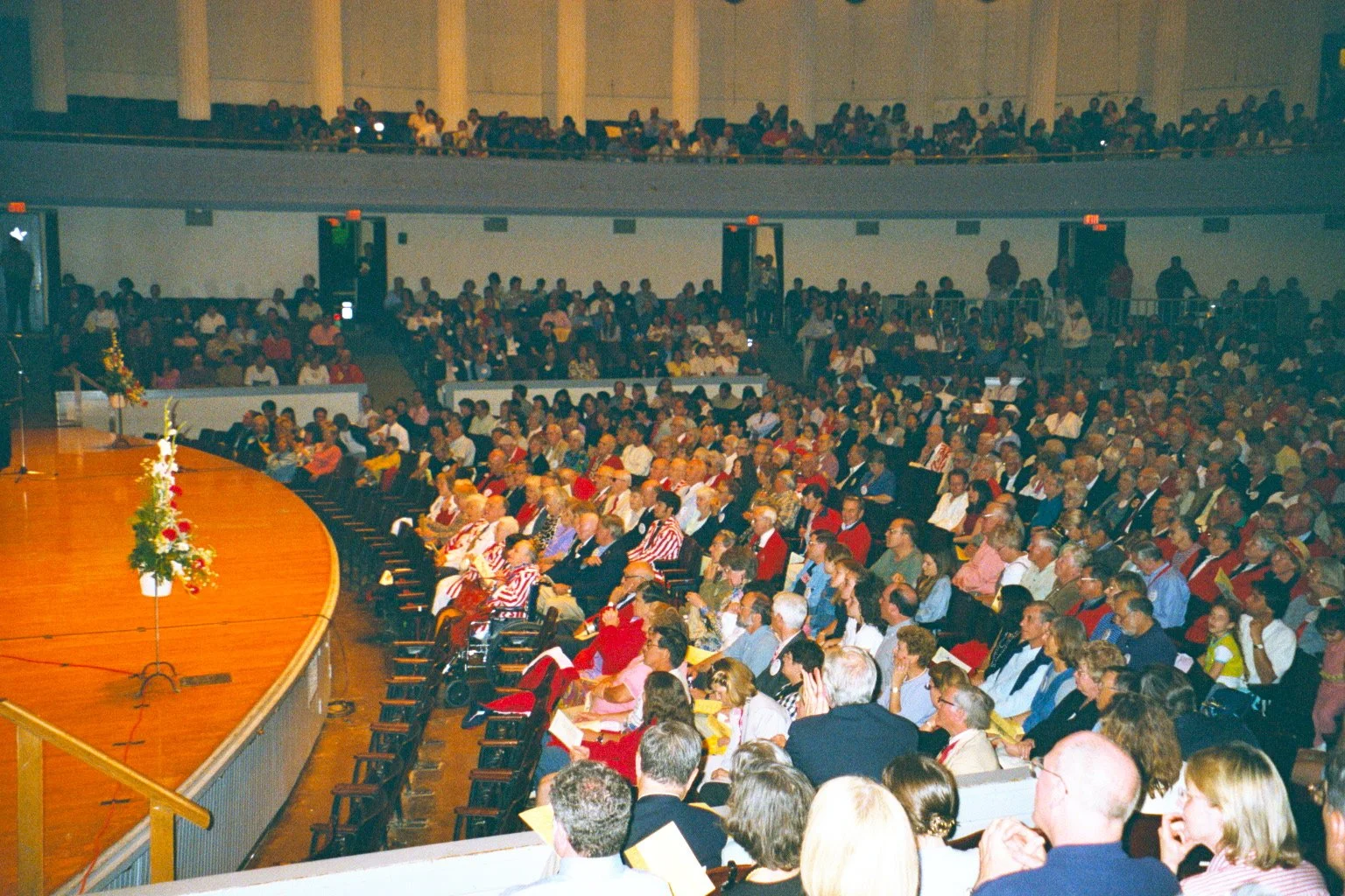 Bailey Hall filled with people seated in chairs, attending a formal event or conference, with a stage on the left side decorated with flowers.