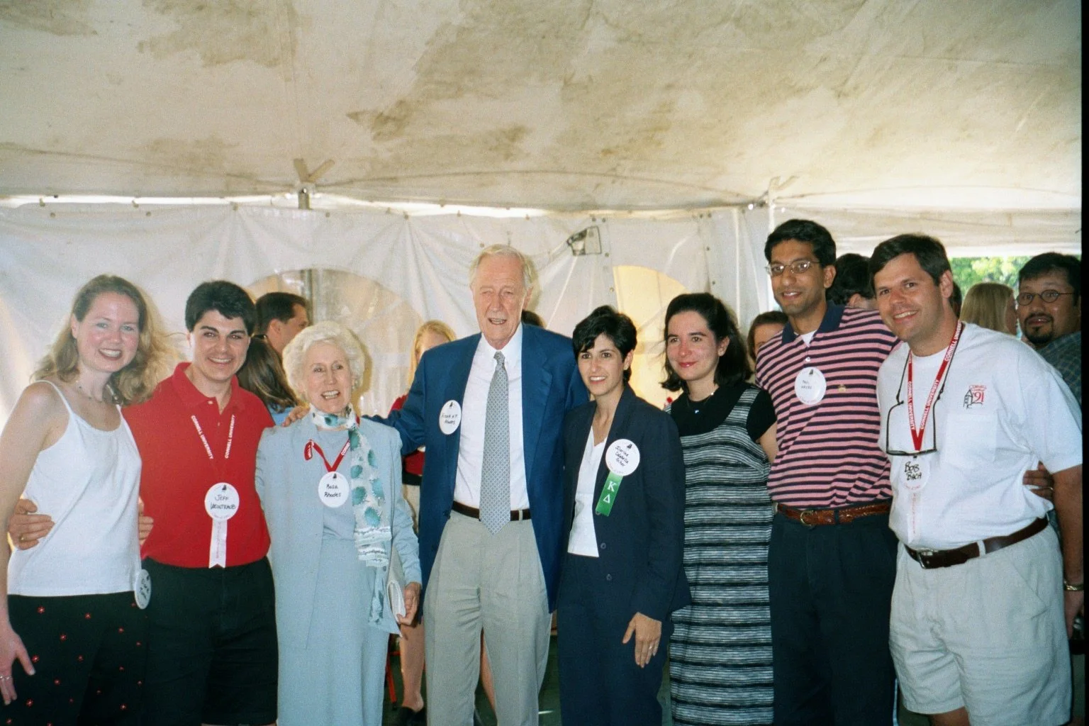 Group of diverse people smiling and posing together at an event, standing inside a tent with a white backdrop.