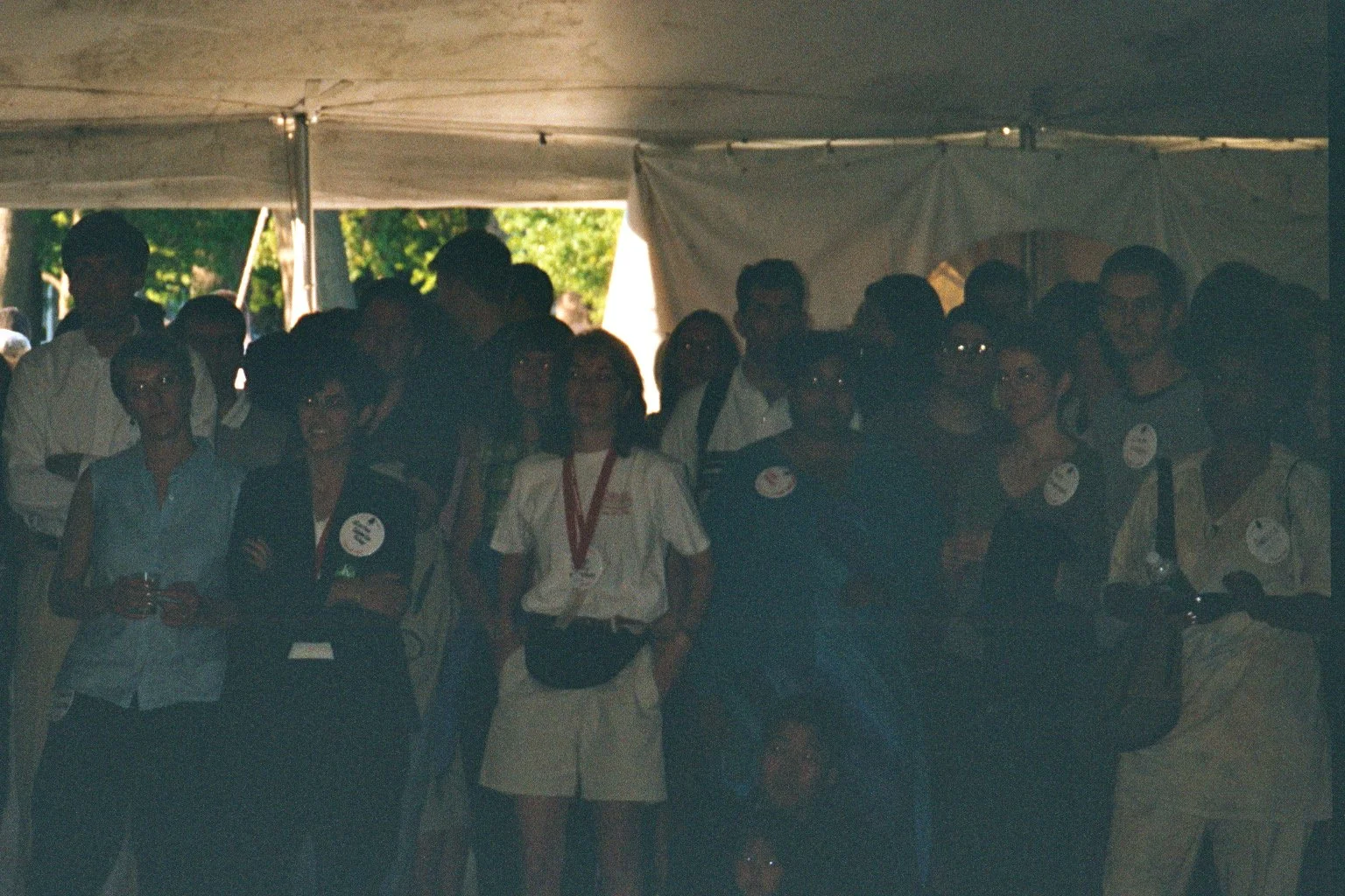 Group of people gathered under a tent at an outdoor event, some wearing name tags and medals.