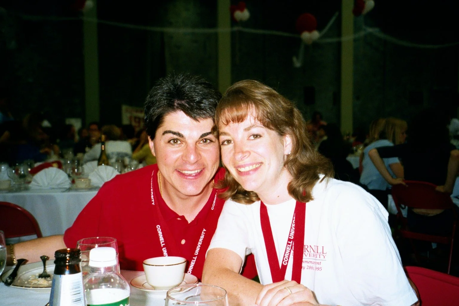 Jeff and Robyn smiling in a banquet hall, wearing Cornell University lanyards, with tables and other guests in the background.