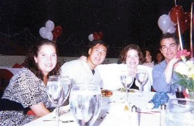 Four people sitting at a dinner table with wine glasses and balloons in the background, celebrating a special occasion.