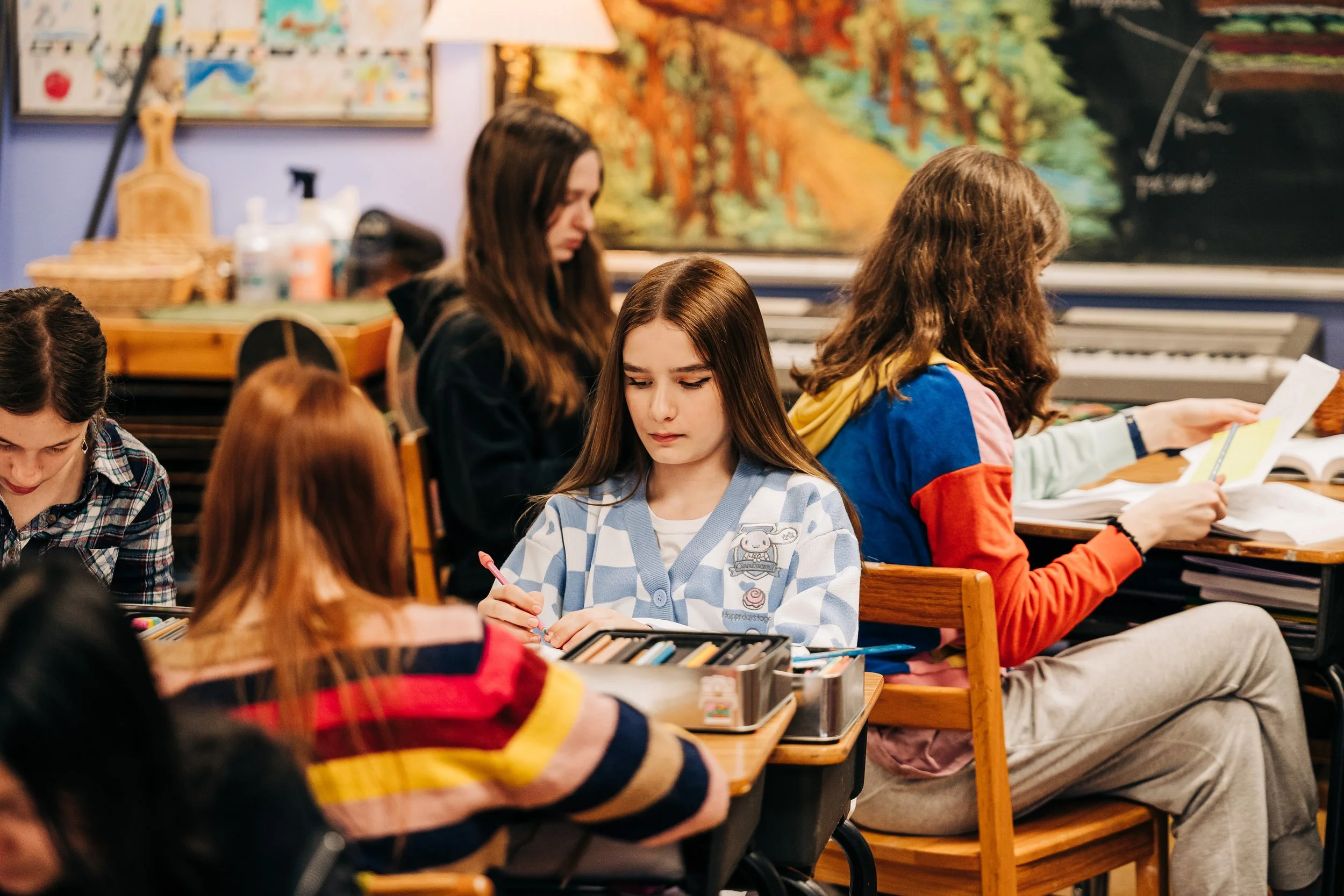 A classroom full of students sitting at desks, studying and reading, with a blackboard and artwork on the wall in the background.