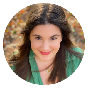 Jeune femme avec cheveux bruns, portant un haut vert, souriant à la caméra, avec un fond flou d'automne.