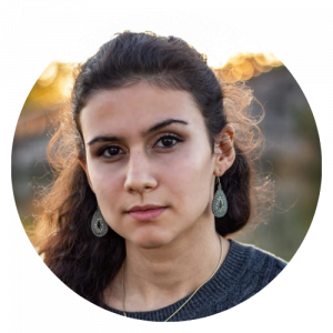 Portrait d'une jeune femme avec des cheveux bouclés, portant des boucles d'oreilles en forme de goutte, en extérieur par une journée ensoleillée.