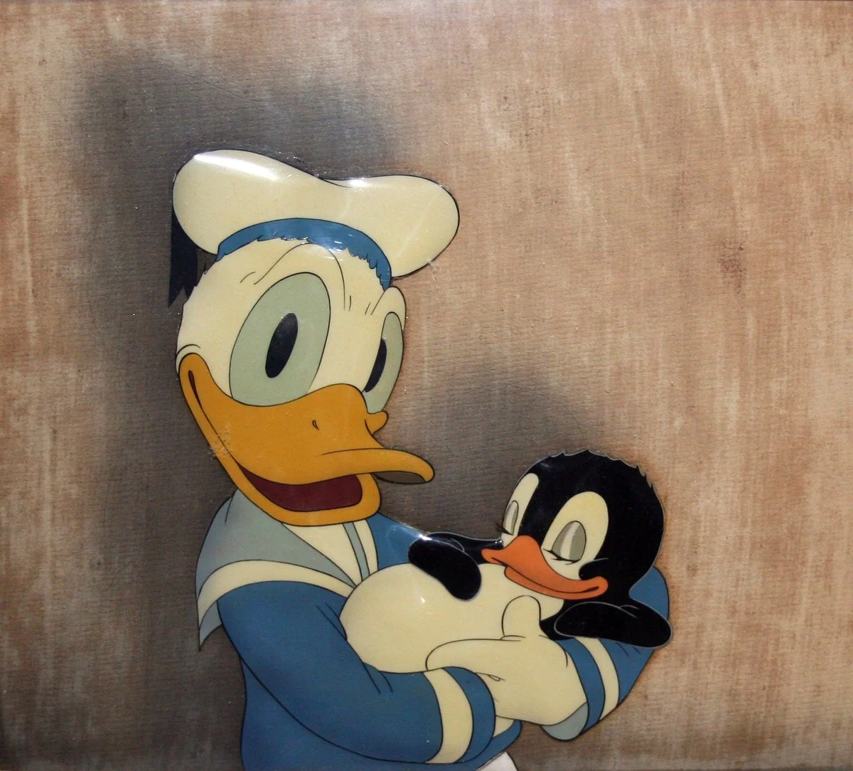 A metal wall decoration of Donald Duck holding a cute, sleepy penguin.