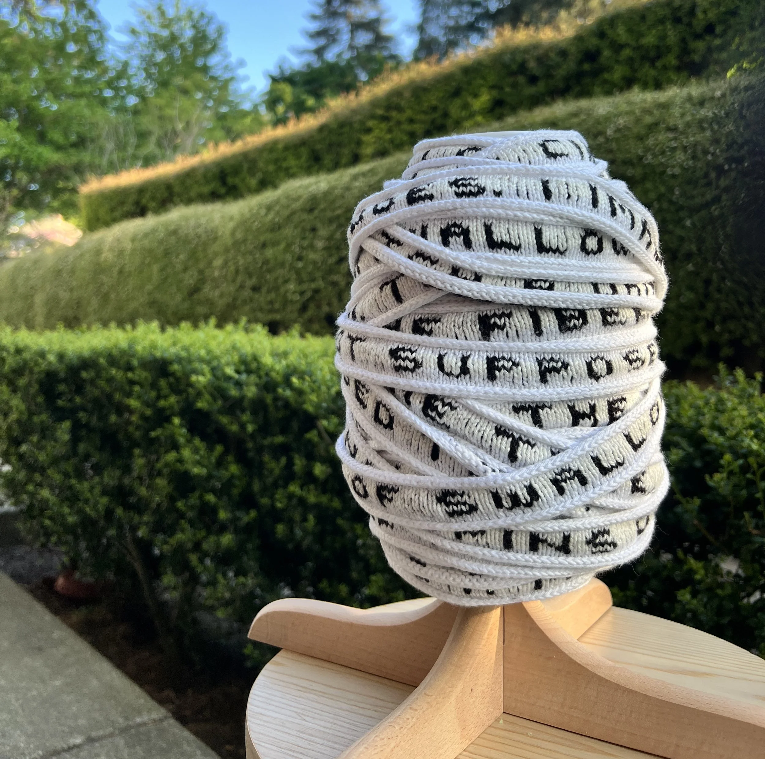 Photograph of knit ribbon on wooden spool, with greenery in the background.