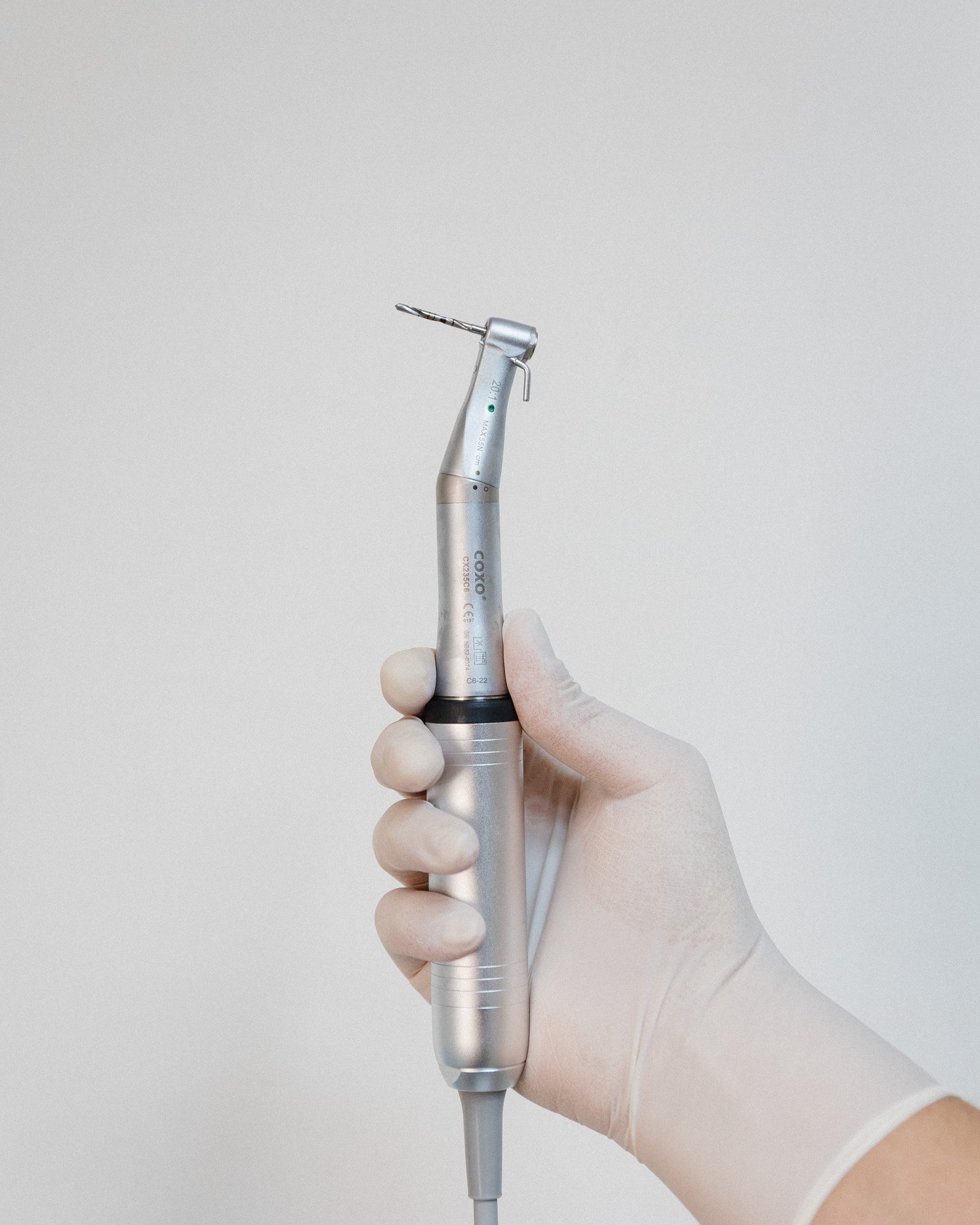 Mano con guante sosteniendo un instrumento dental de color plateado