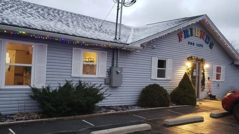 A small community building decorated with holiday lights and Christmas greenery, with a sign that reads 'Friends for Life.'