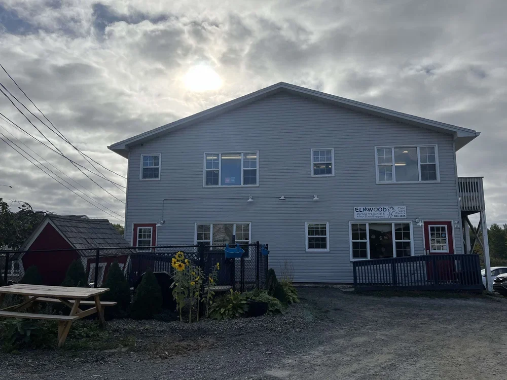 Two-story light gray building with a sign for Elmwood Child Care in a partly cloudy sky