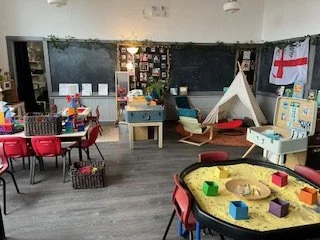 Classroom with blackboard, small tent, and various toys and furniture for young children.