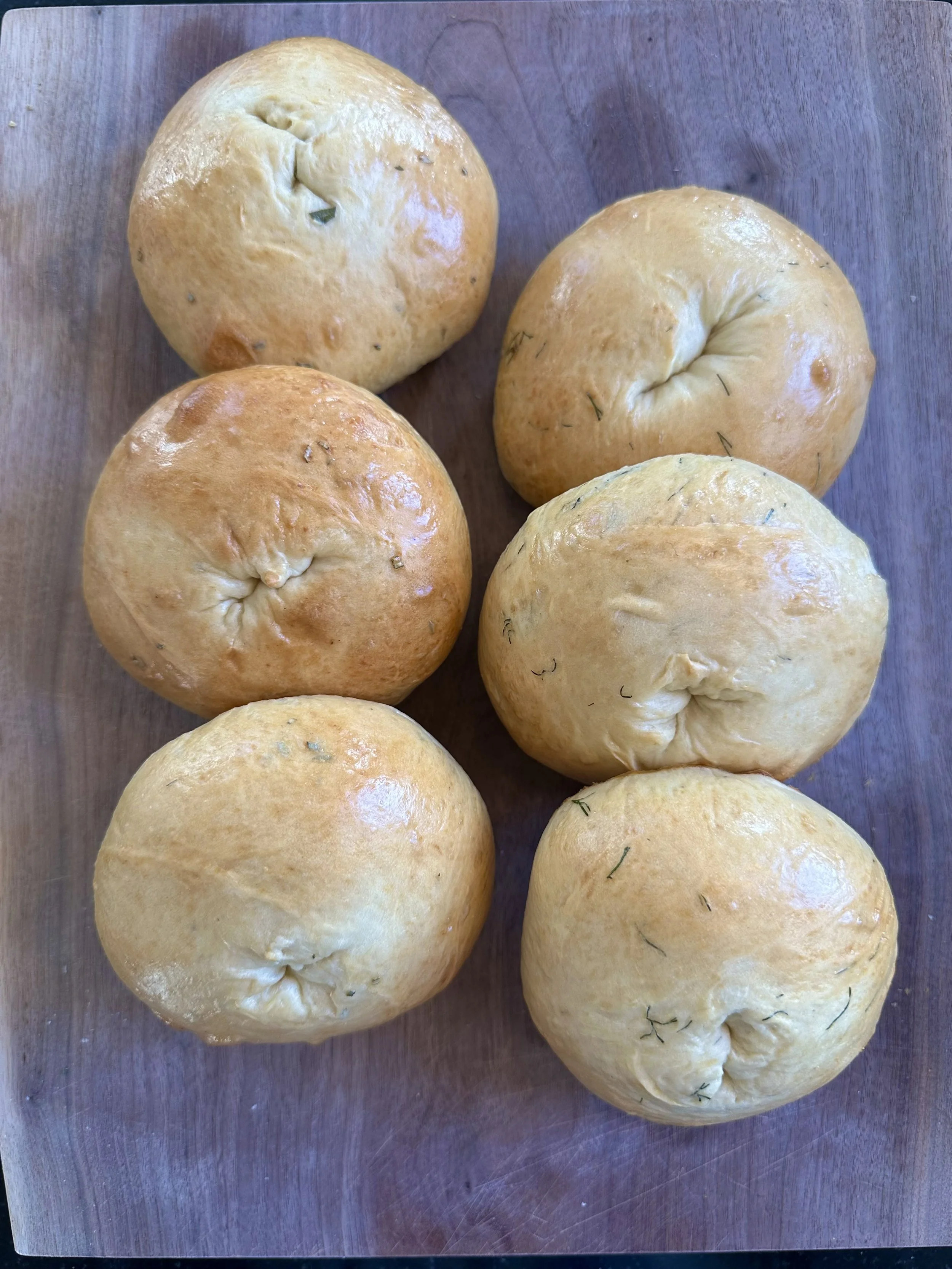 Six bagels  with herbs on a wooden surface.