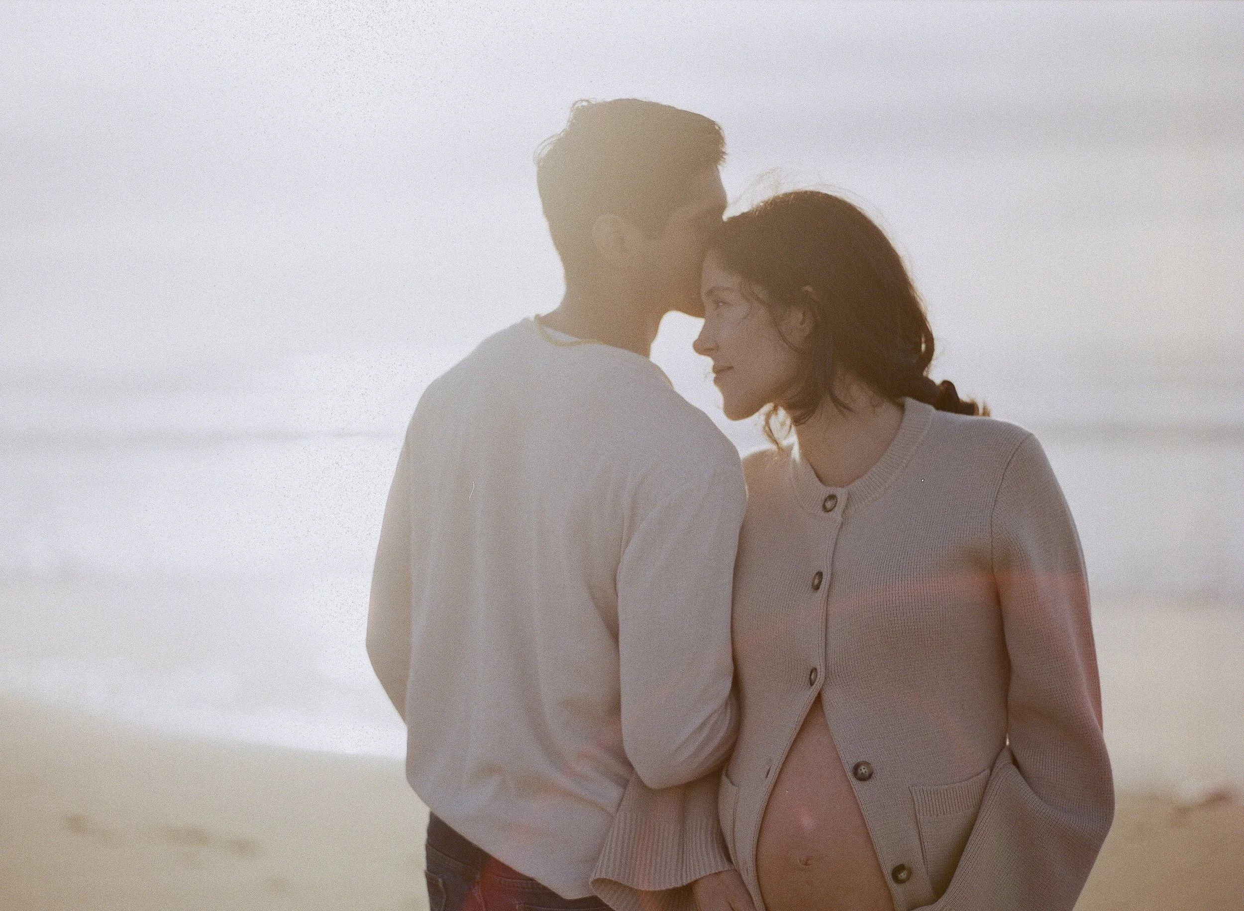 Couple in golden light on the beach, woman pregnant, absorbed in each other — Radostina Boseva film maternity photographer San Francisco