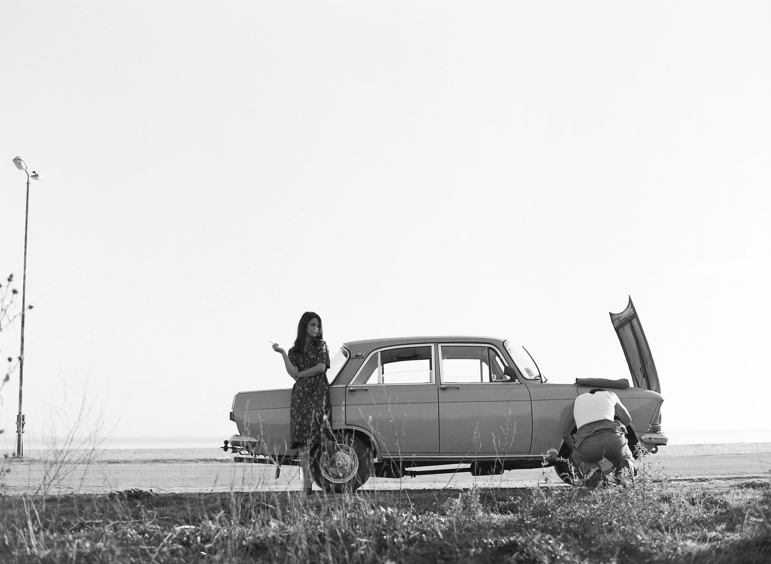 wo figures beside a broken-down car on an empty road, rural Bulgaria — Radostina Boseva Still Here film photography