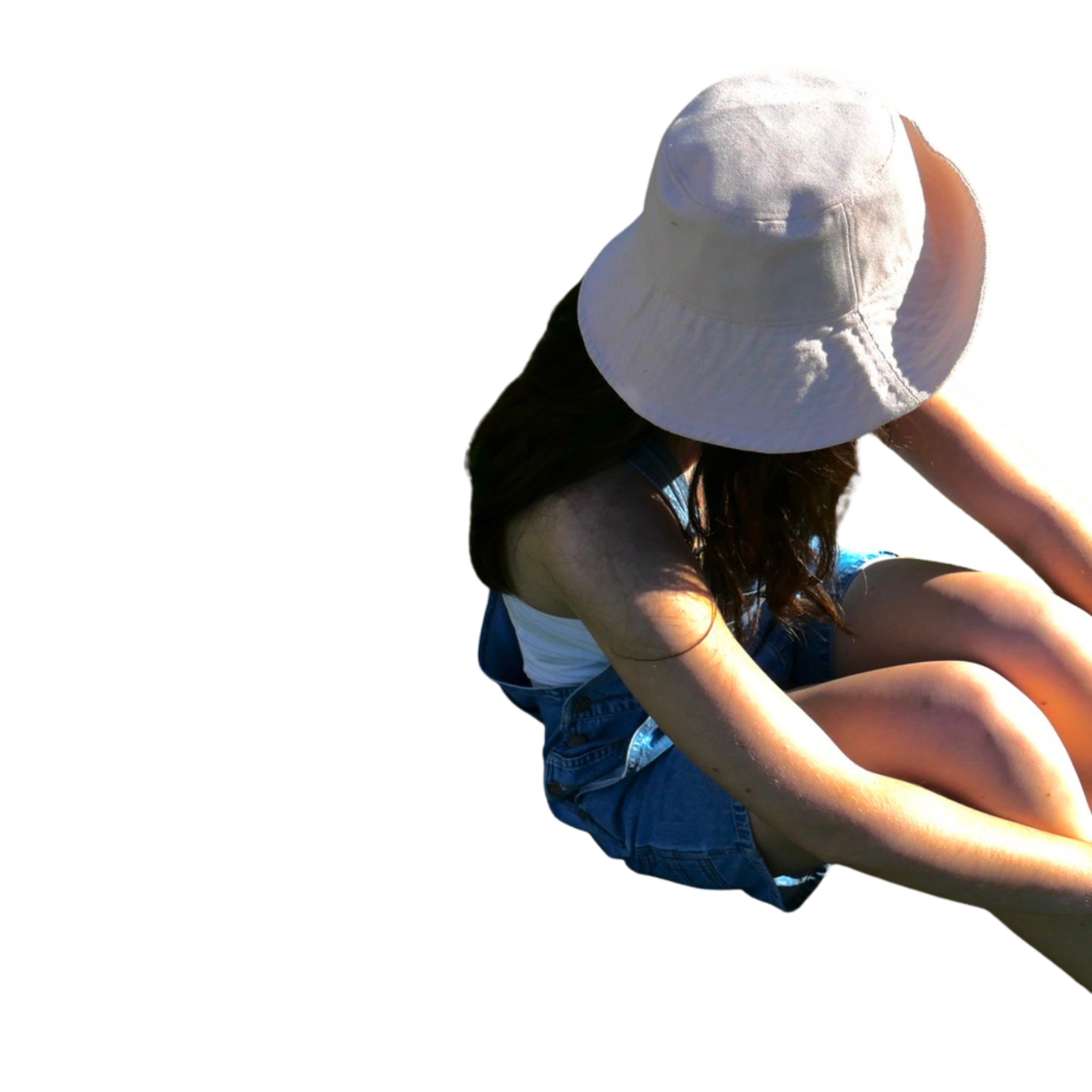 A woman wearing a white sun hat, white tank top, and denim shorts sitting on the ground with her knees bent, outdoors in sunlight.
