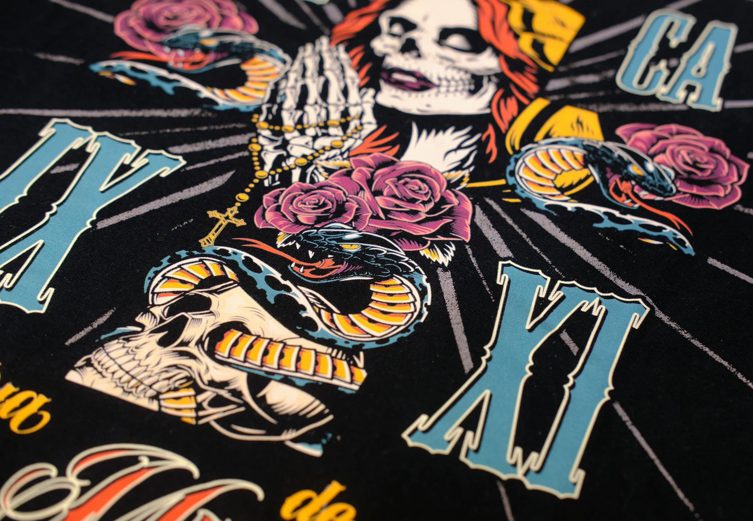 Close-up of a graphic design featuring a woman with a skeleton face holding a rosary, surrounded by roses, with the words 'LA CA' and other partially visible text in bright colors on a dark background.
