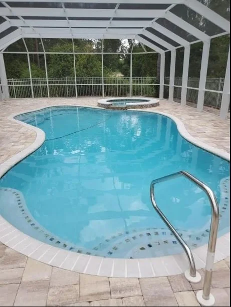 An indoor swimming pool with a hot tub in a screened enclosure.