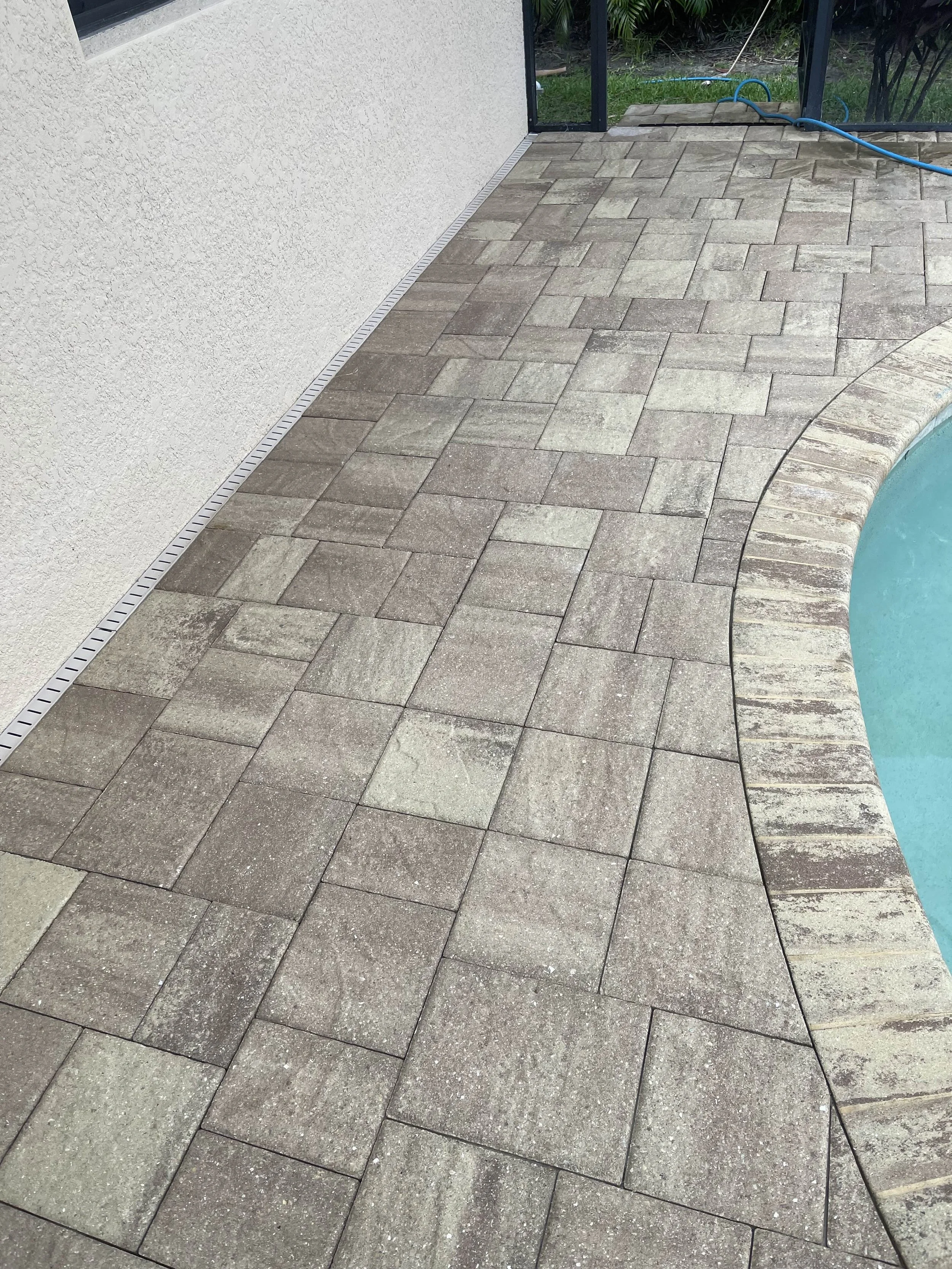 Concrete pool deck with patterned pavers next to a swimming pool.