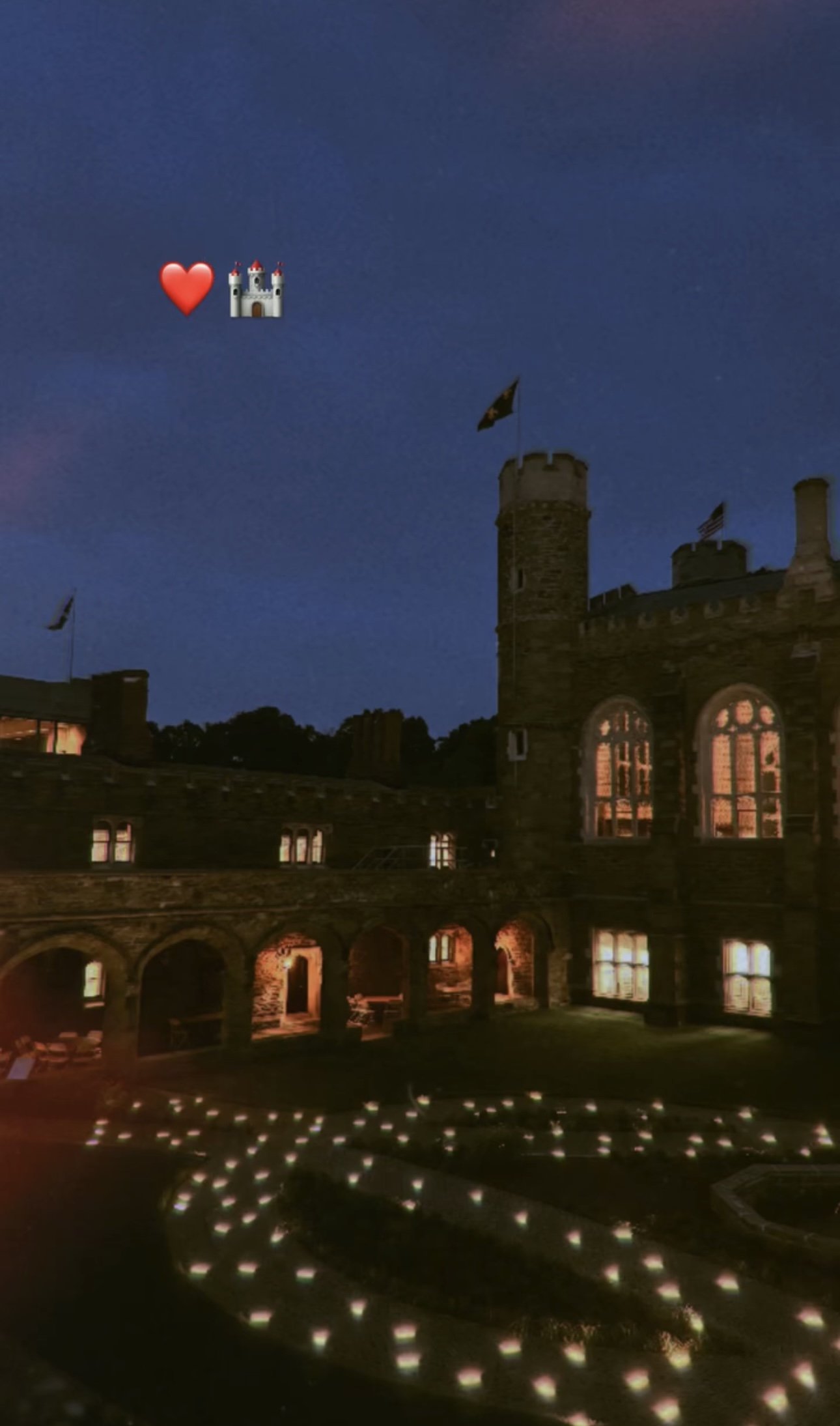 A castle at night with lit windows and a dark blue sky, decorated with a heart and castle emoji in the sky.