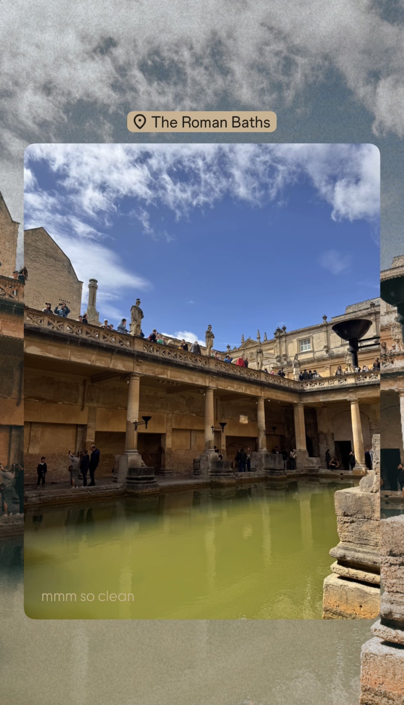 The Roman Baths, historical site with ancient architecture, stone pillars, tiered walkways, and a pool of greenish water, with numerous visitors exploring the area under a partly cloudy sky.