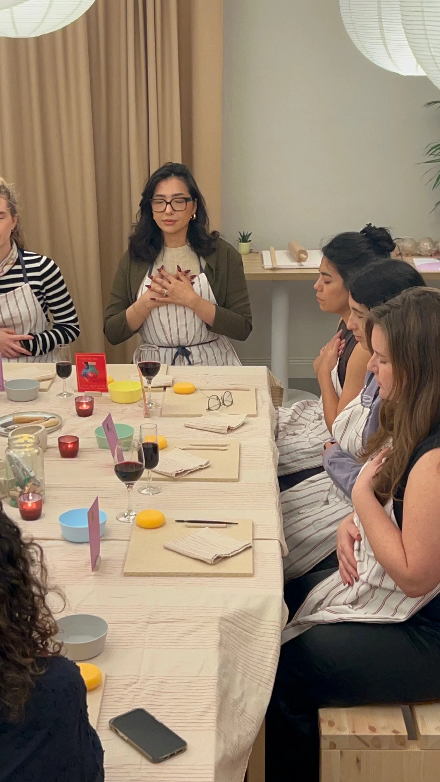 Women participating in a cooking or baking class, with ingredients, utensils, and wine glasses on the table.