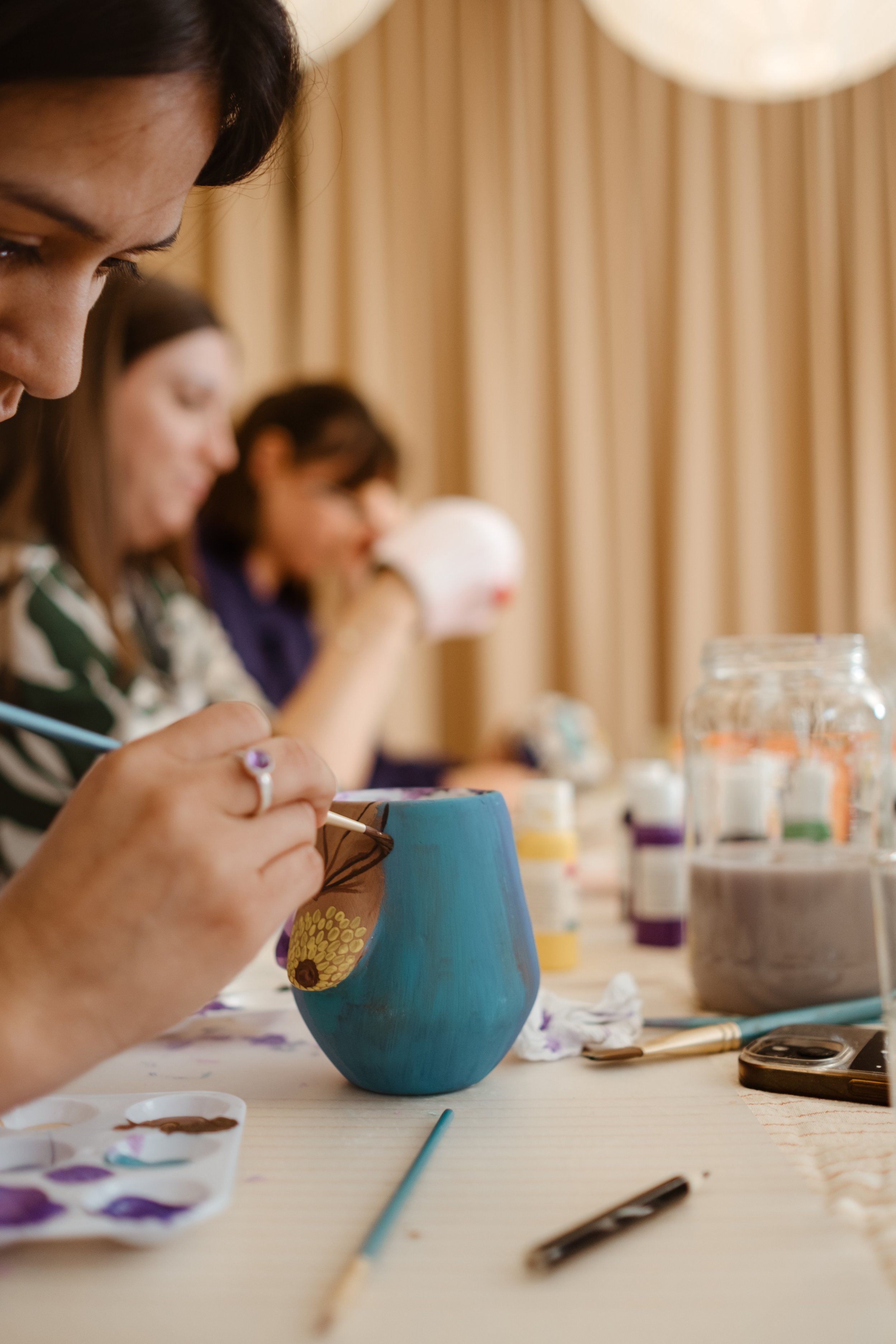 Women painting designs on ceramic pottery at a table during a craft workshop.