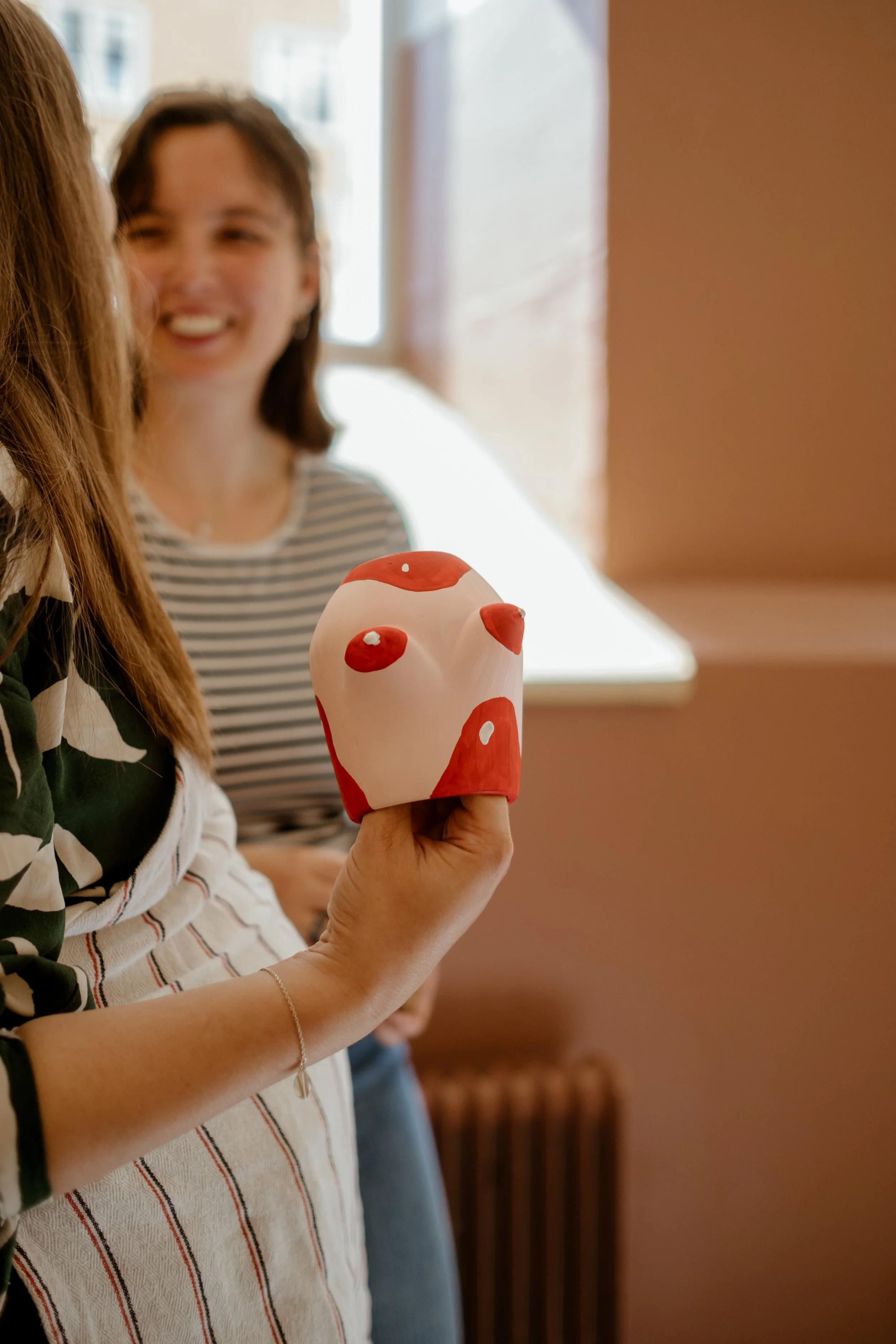 Person holding a red and white mushroom-shaped object, with a woman smiling in the background.