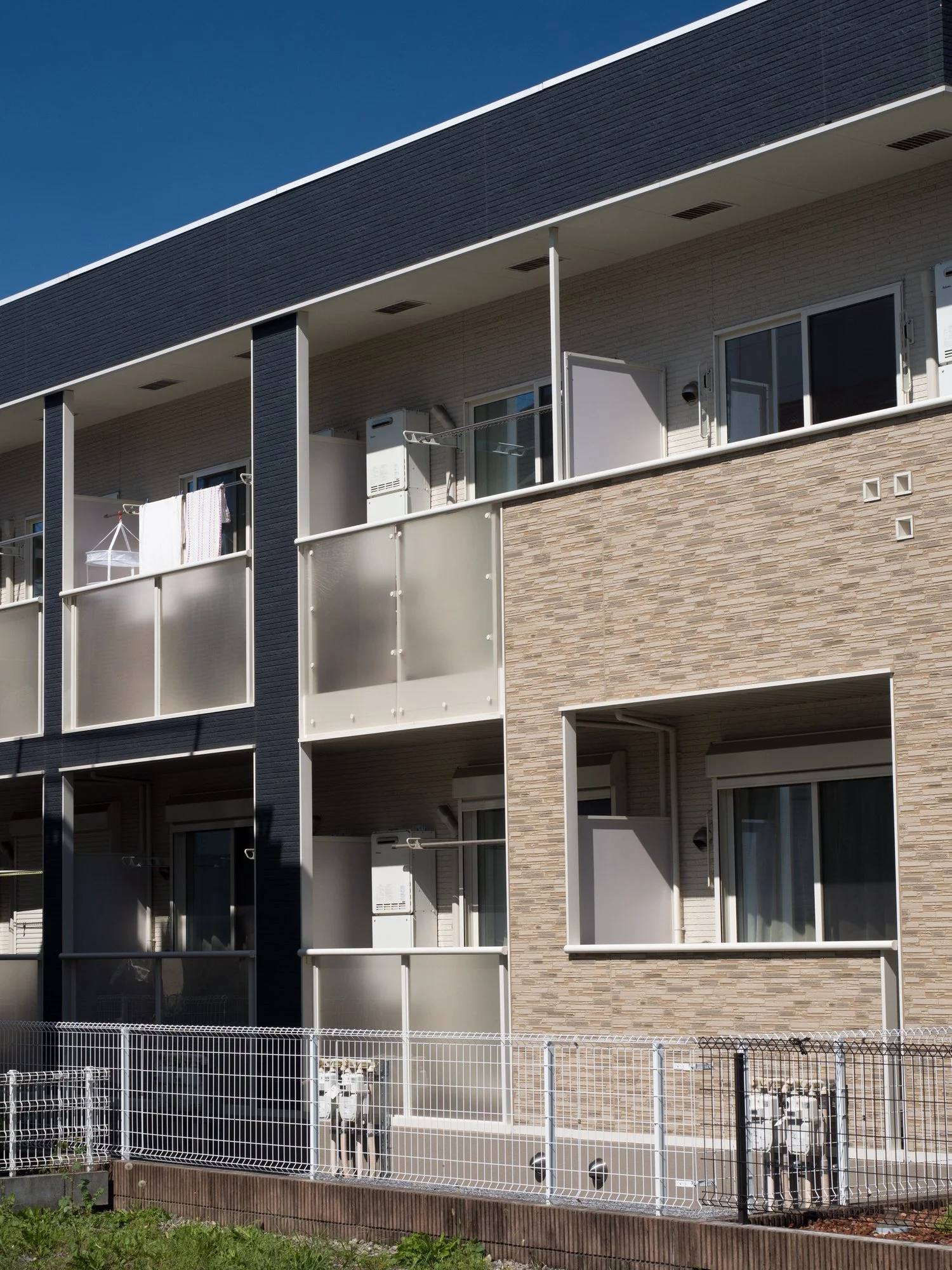 Close-up of the exterior of a modern apartment building with balconies, glass railings, and a mix of dark and light external wall materials.