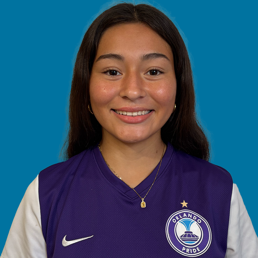 A young woman smiling, wearing a purple Orlando Pride sports jersey with a team logo and a star above it, set against a blue background.