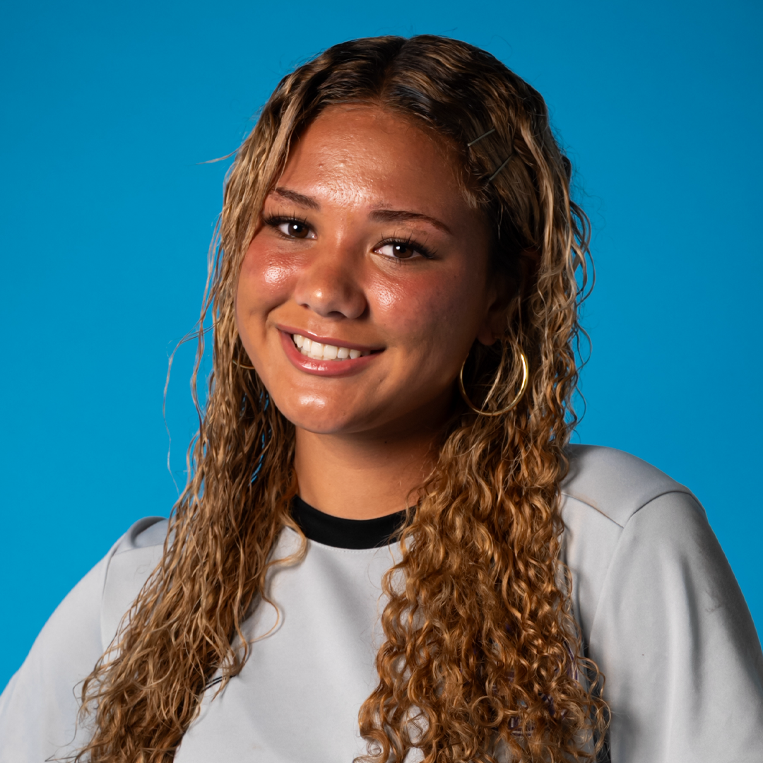 A young woman with light brown curly hair smiling against a blue background.