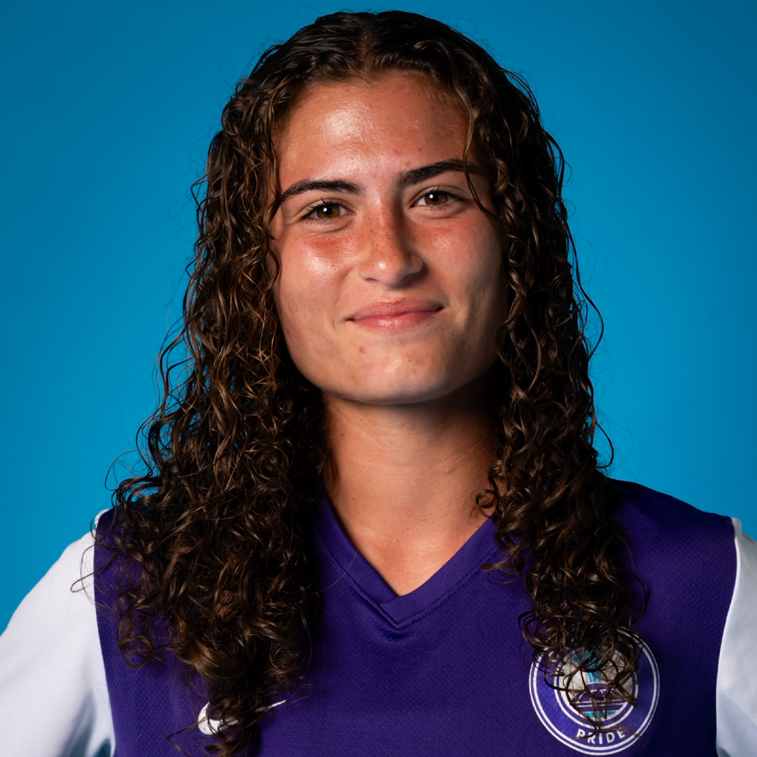 Young woman with curly brown hair wearing a purple sports jersey with a logo, smiling slightly against a blue background.