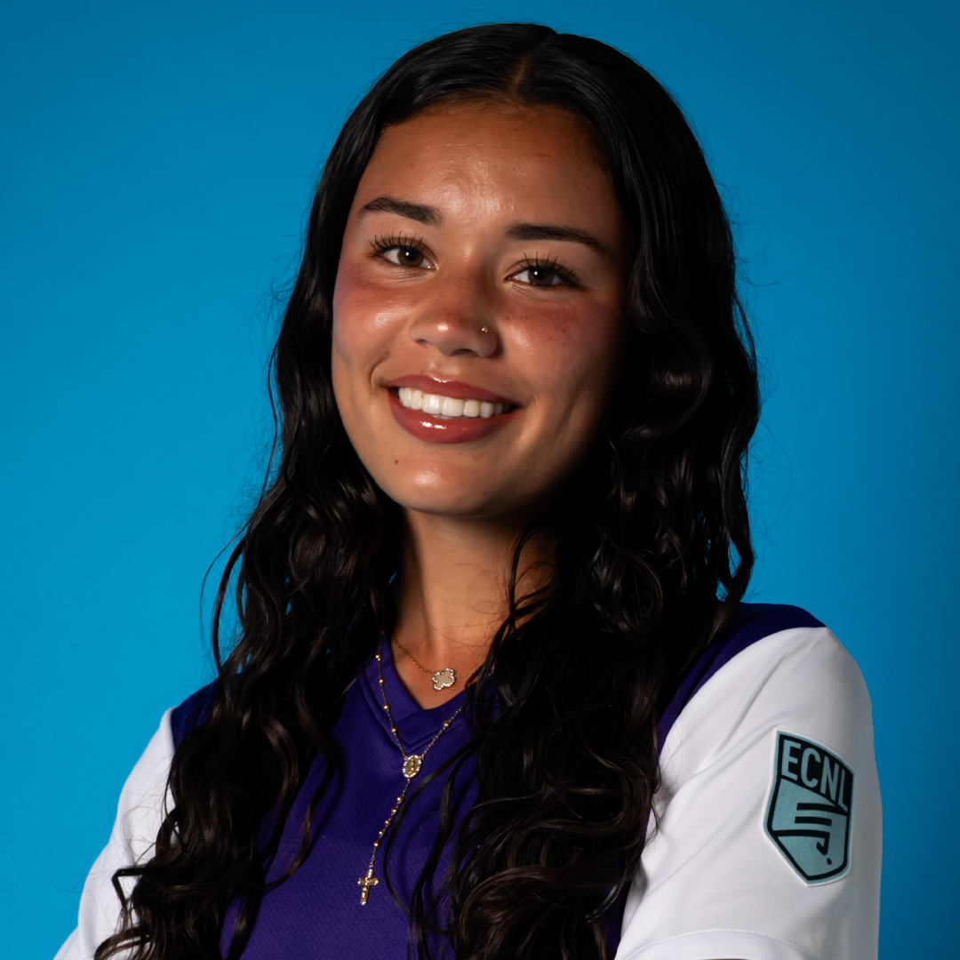 A young woman with dark, wavy hair, wearing a white and purple sports jersey with an ECNL patch on the sleeve, smiling against a blue background.