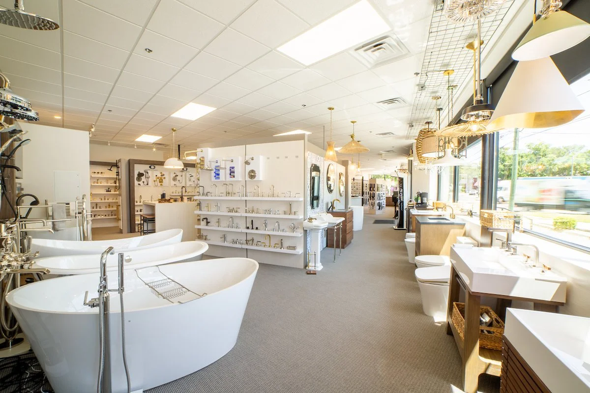Showroom of sinks, faucets, and bathroom fixtures with the store interior and large windows showing outside view.
