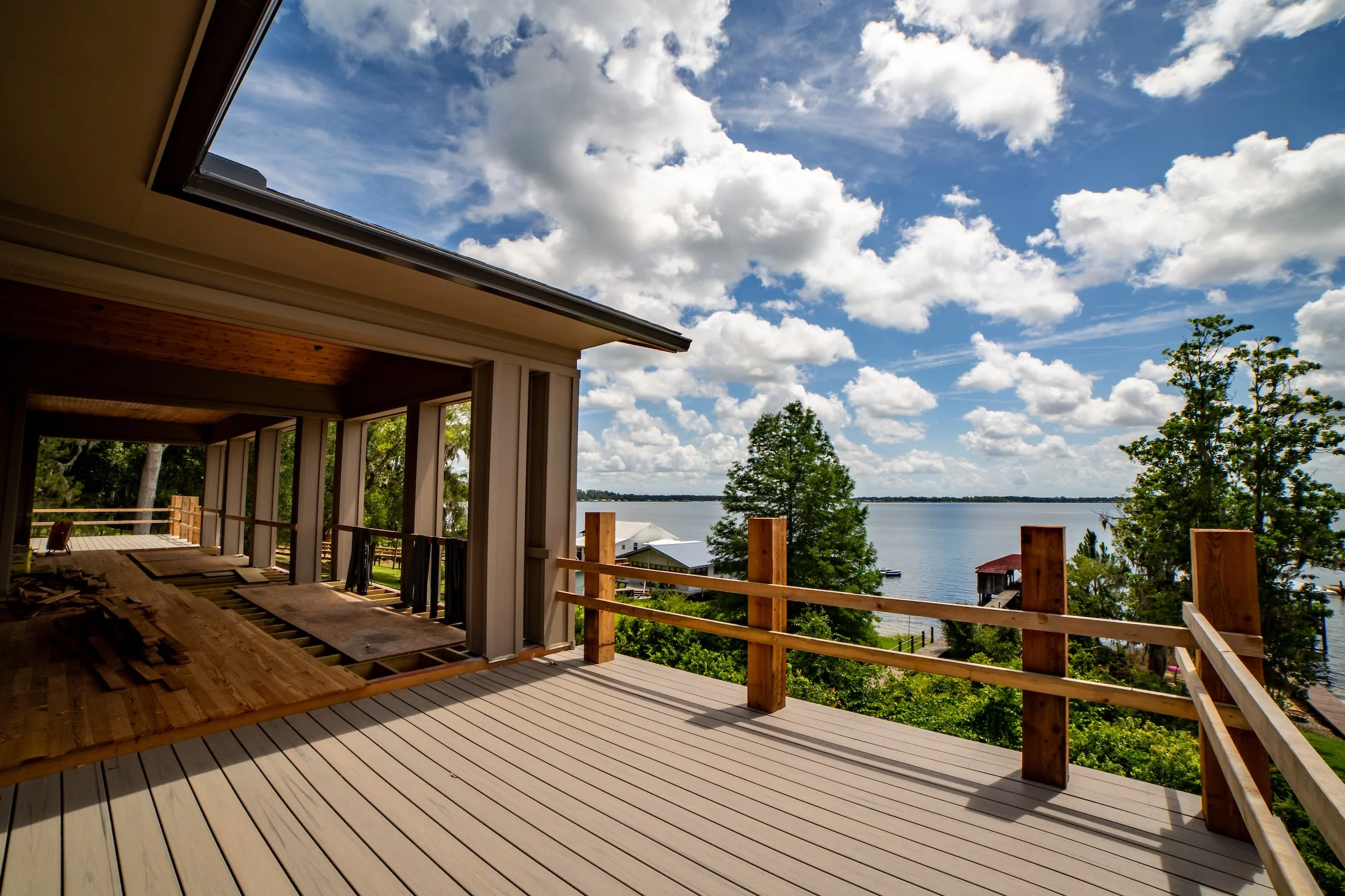 View from an unfinished house balcony overlooking a lake with trees and houses, under a partly cloudy sky.