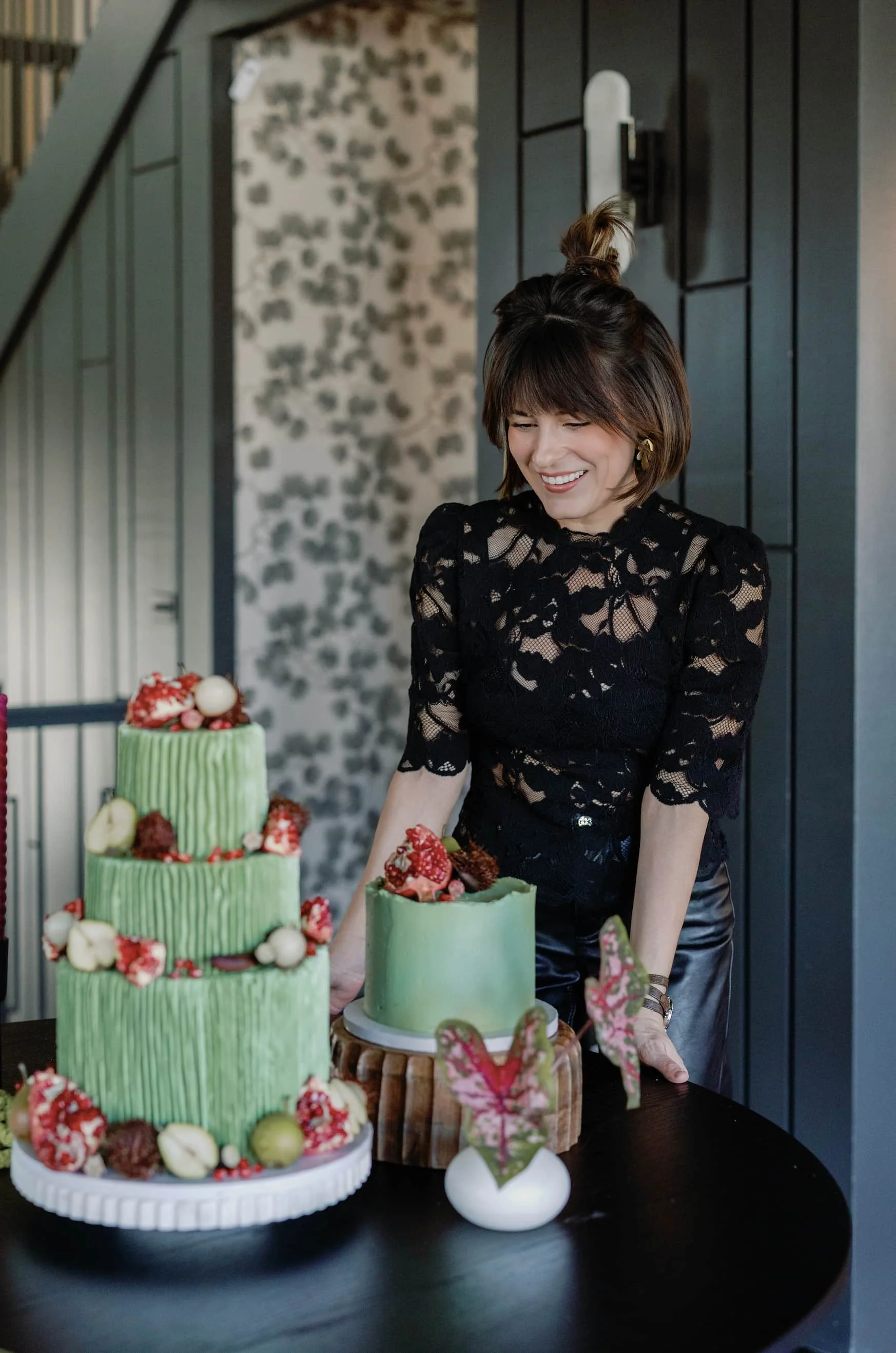 Danielle of Futtitinni Events styling a modern green wedding cake with floral details during an event design setup