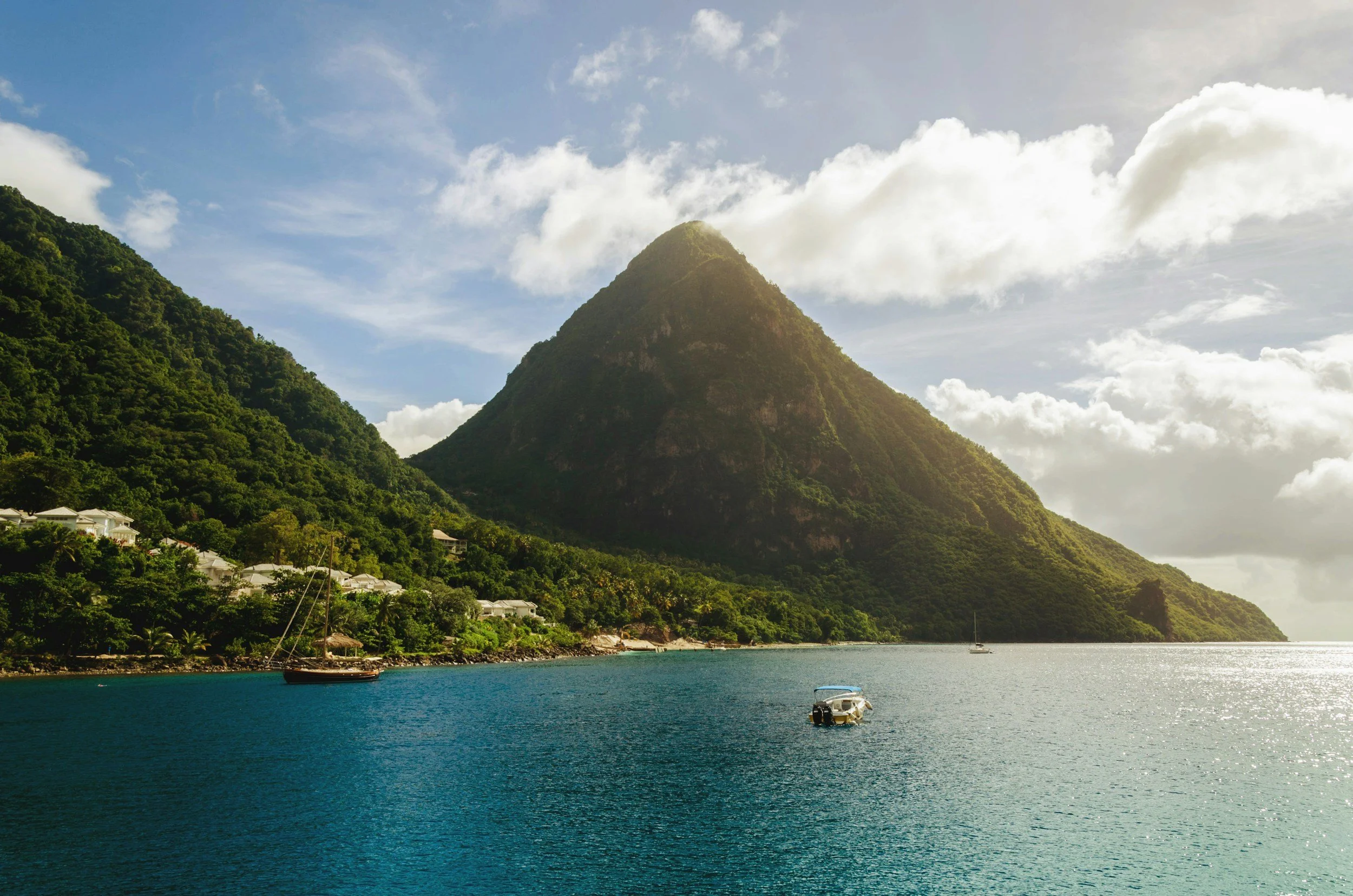 A scenic view of a mountain covered in greenery overlooking a calm water body with boats and a coastal area with houses.