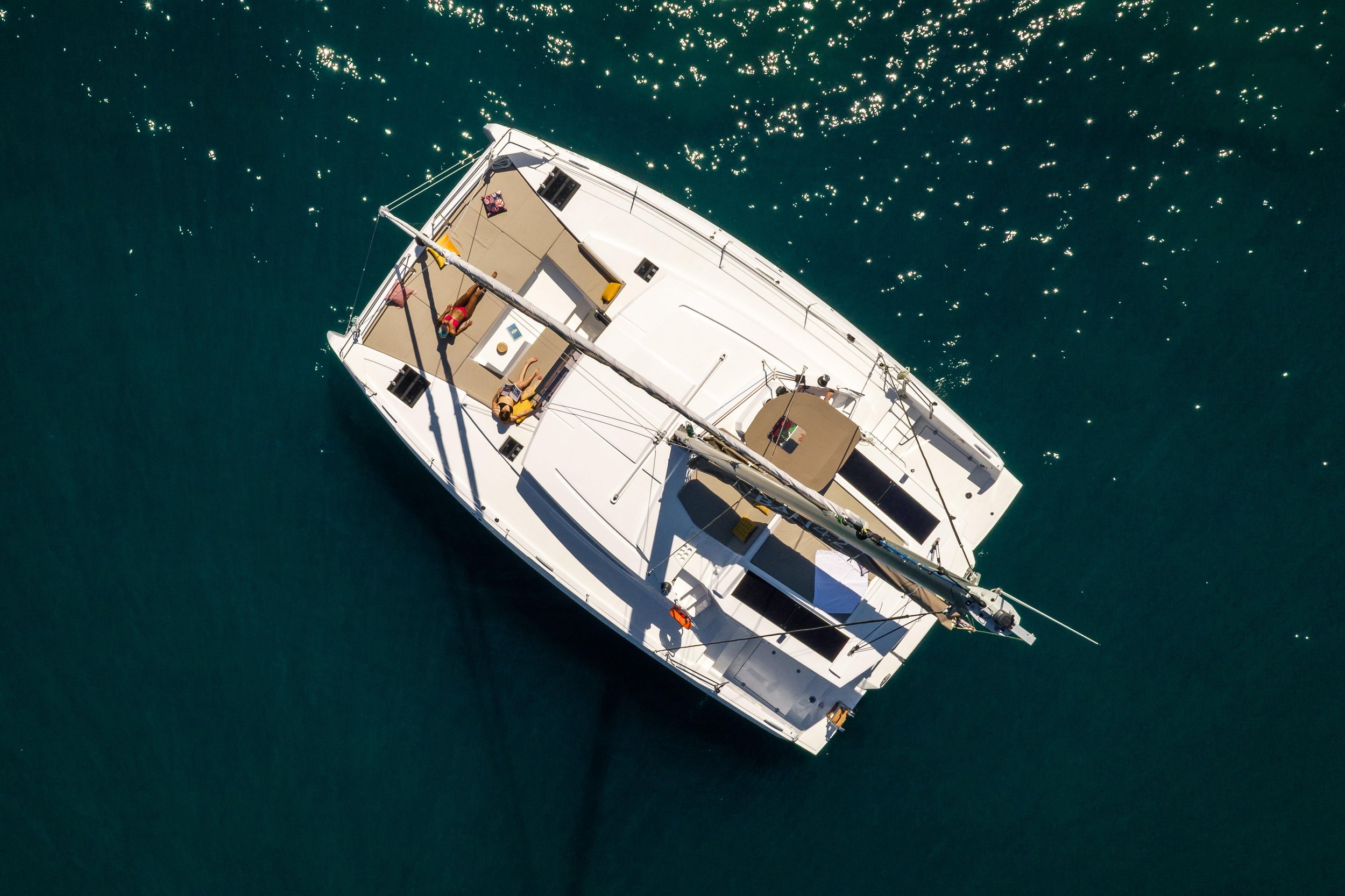 Aerial view of a white yacht on dark blue water with two people relaxing on deck.