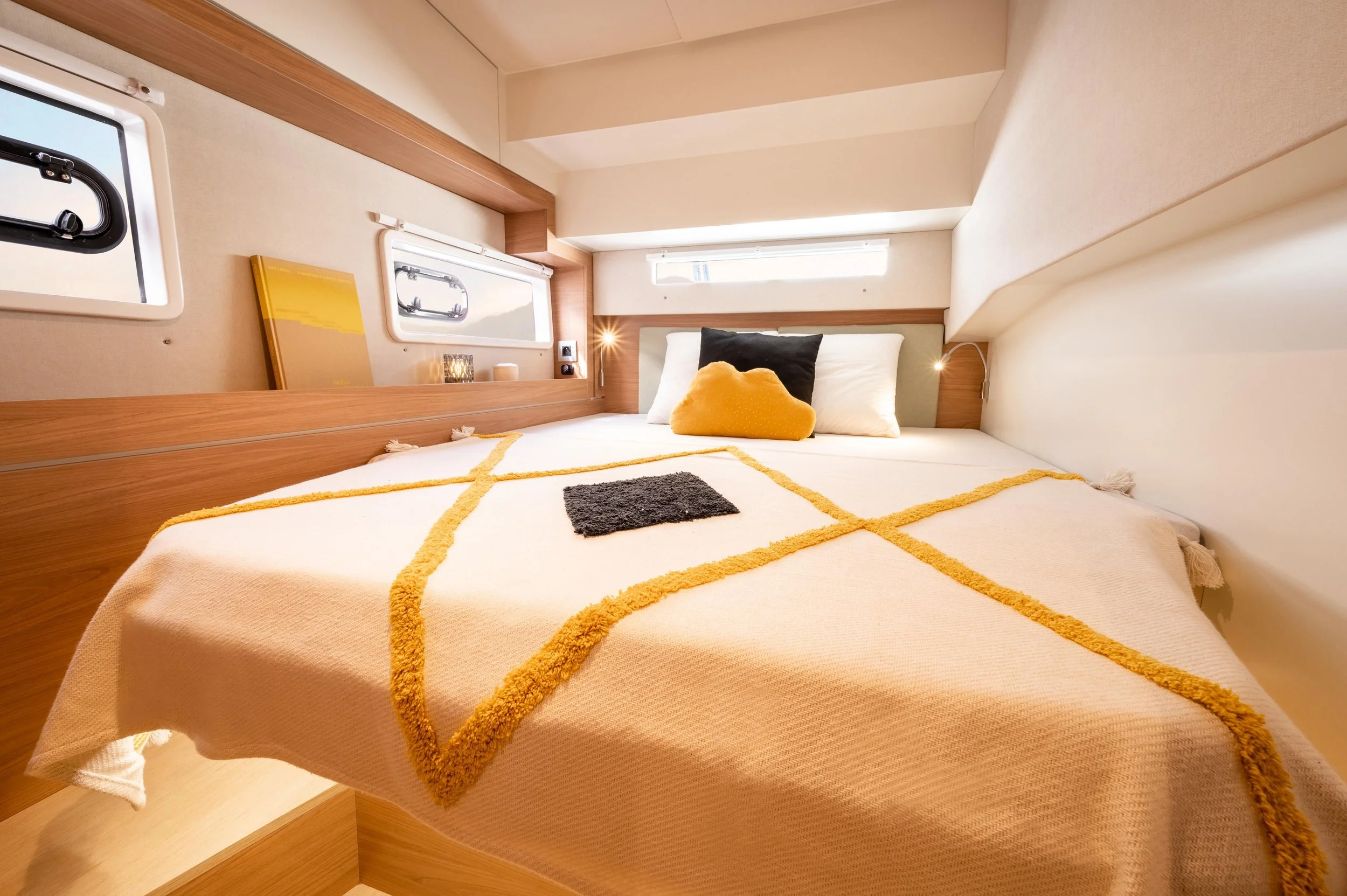 Cozy bedroom with a neatly made bed, black and yellow pillows, and small windows letting in natural light.