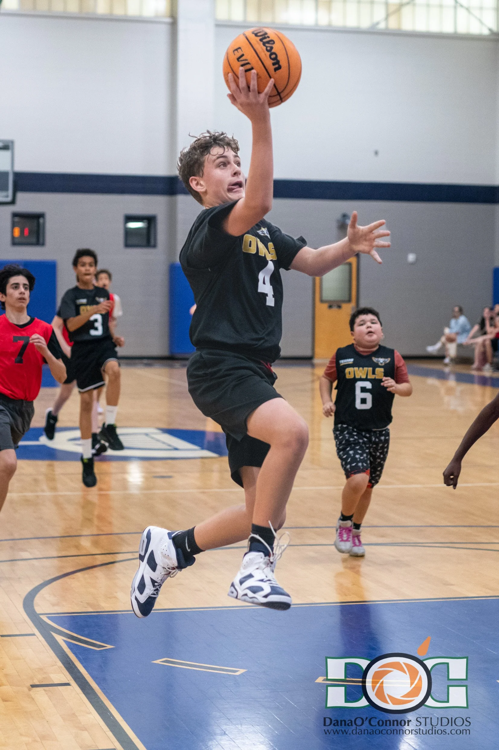 Orlando Gifted Academy player on the 8th Grade basketball team in black sports uniform playing basketball indoors, takes the ball to the hole while other watch in the background.