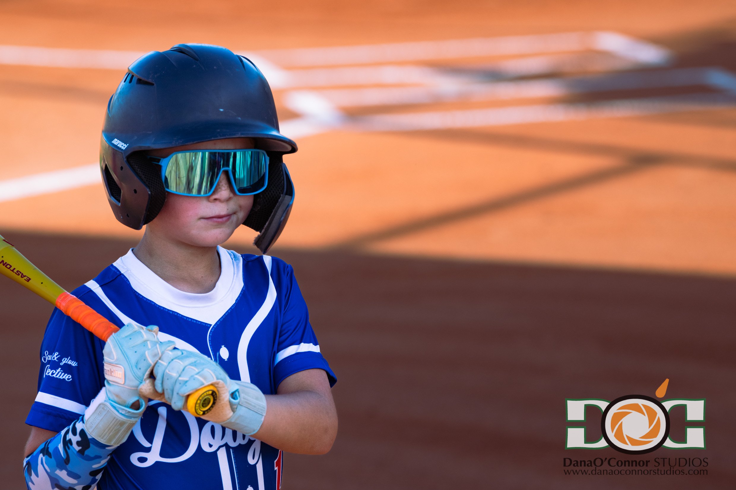 Apopka Little League 9U Dodgers player in a blue uniform and helmet with reflective glasses, holding a yellow bat.
