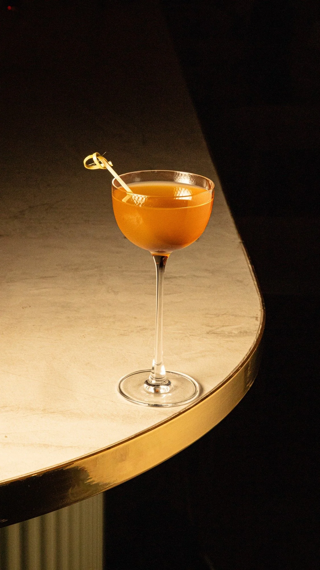 Coctel Santo Viejo en copa coupe, color ámbar con twist de cítrico, en Mecenas Bar