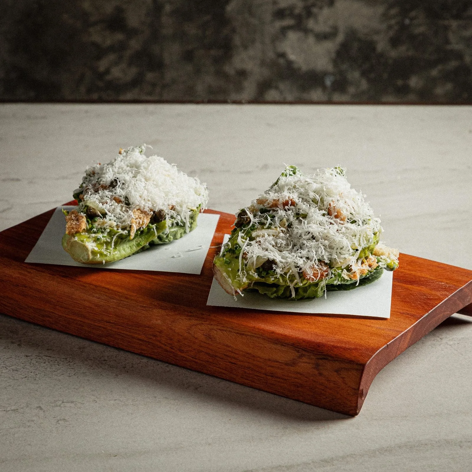 Bocados de ensalada César con queso rallado sobre tabla de madera, botana de Mecenas