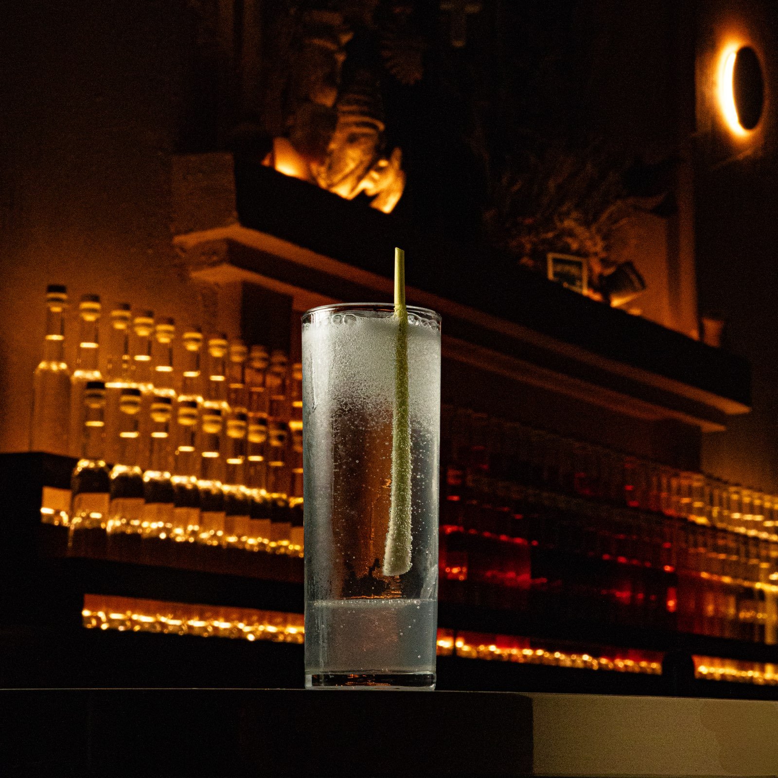 Coctel Lemon Up en vaso alto con hielo frente a la estantería de botellas iluminada