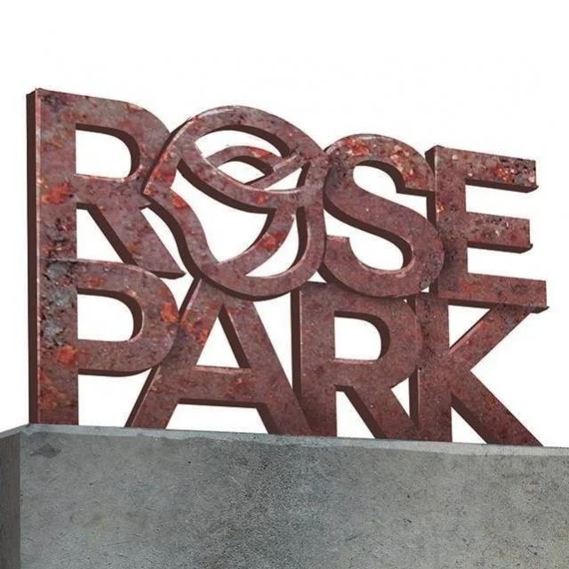 A three-dimensional sign spelling out "ROSE PARK" in large rusted metal letters, with the letter "O" stylized as a rose, mounted on a concrete base.
