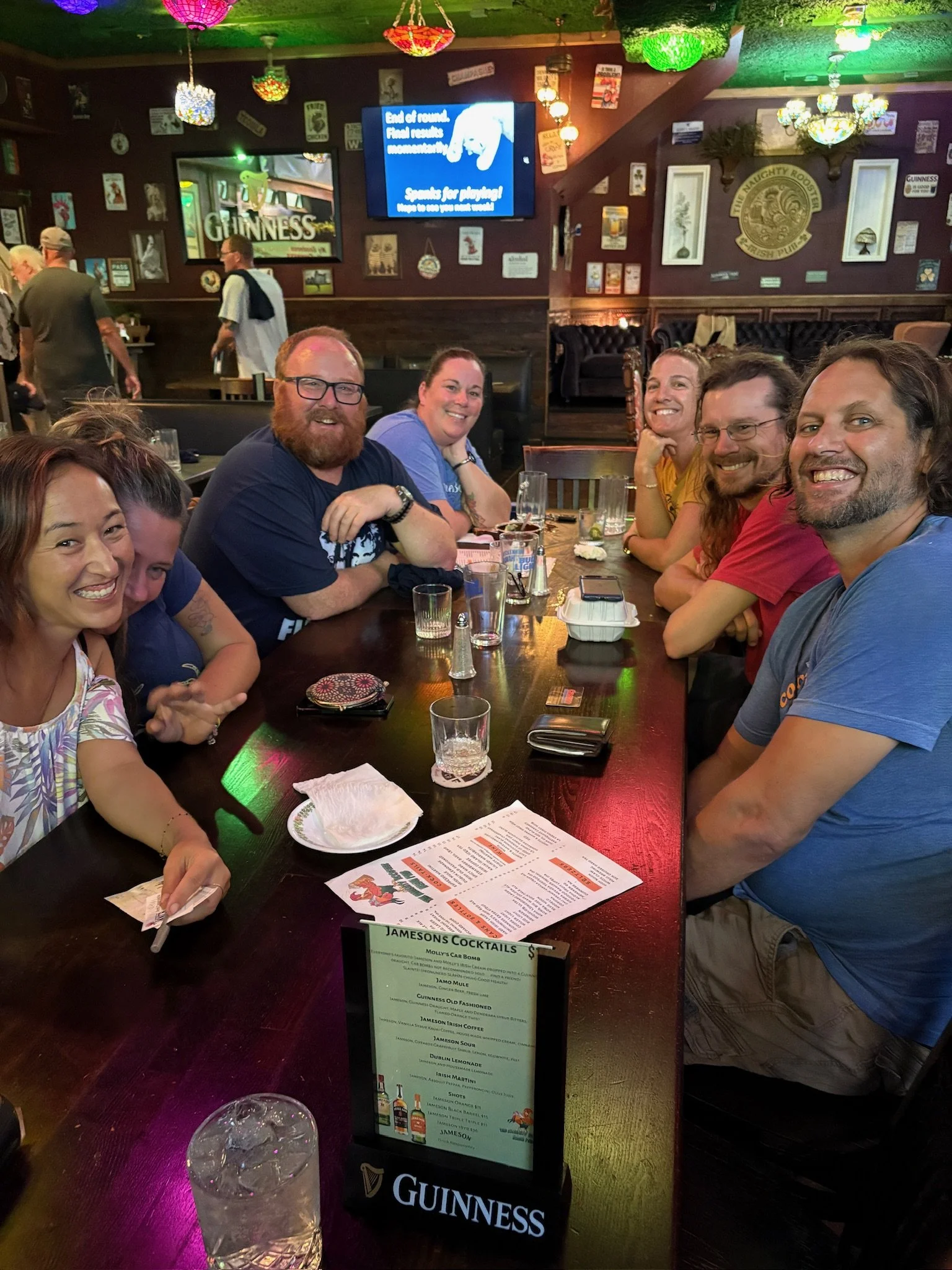 Large group celebrating at The Naughty Rooster Irish Pub in Lihue, Kauai with colorful lighting and lively bar atmosphere.